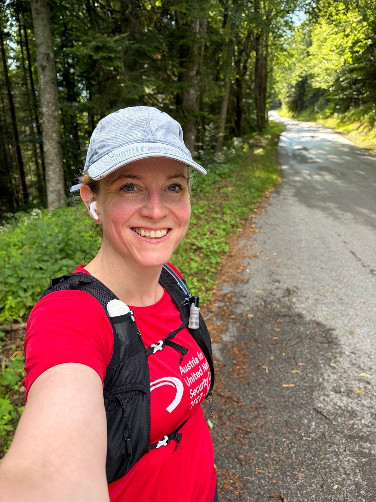 Frau mit rotem Shirt und Kappe macht ein Selfie auf einem Waldweg.