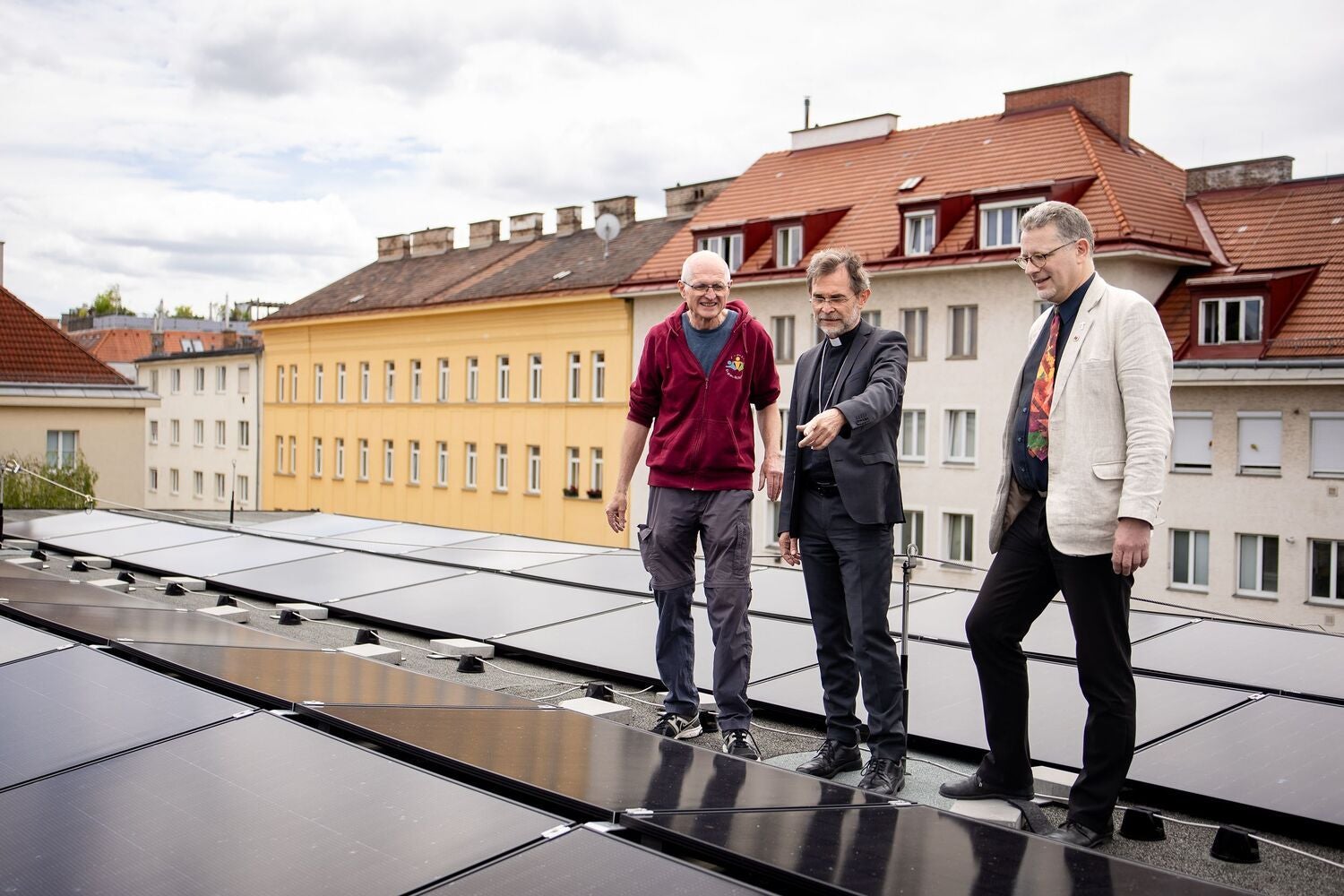 Drei Männer stehen auf einem Dach mit installierten Photovoltaik-Modulen in einer Stadt.