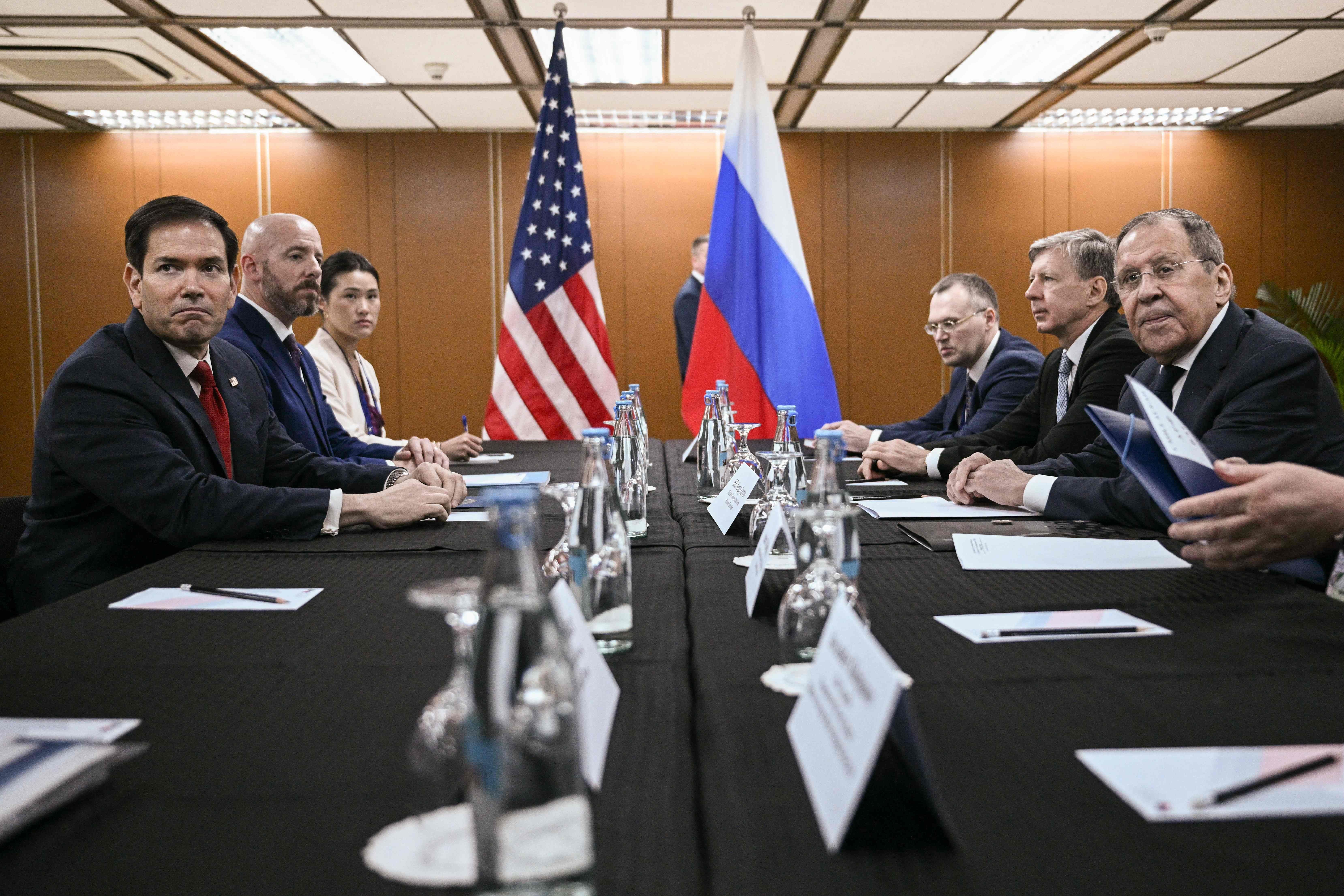 Delegationen der USA und Russlands sitzen sich bei einem Treffen mit Flaggen am Tisch gegenüber.