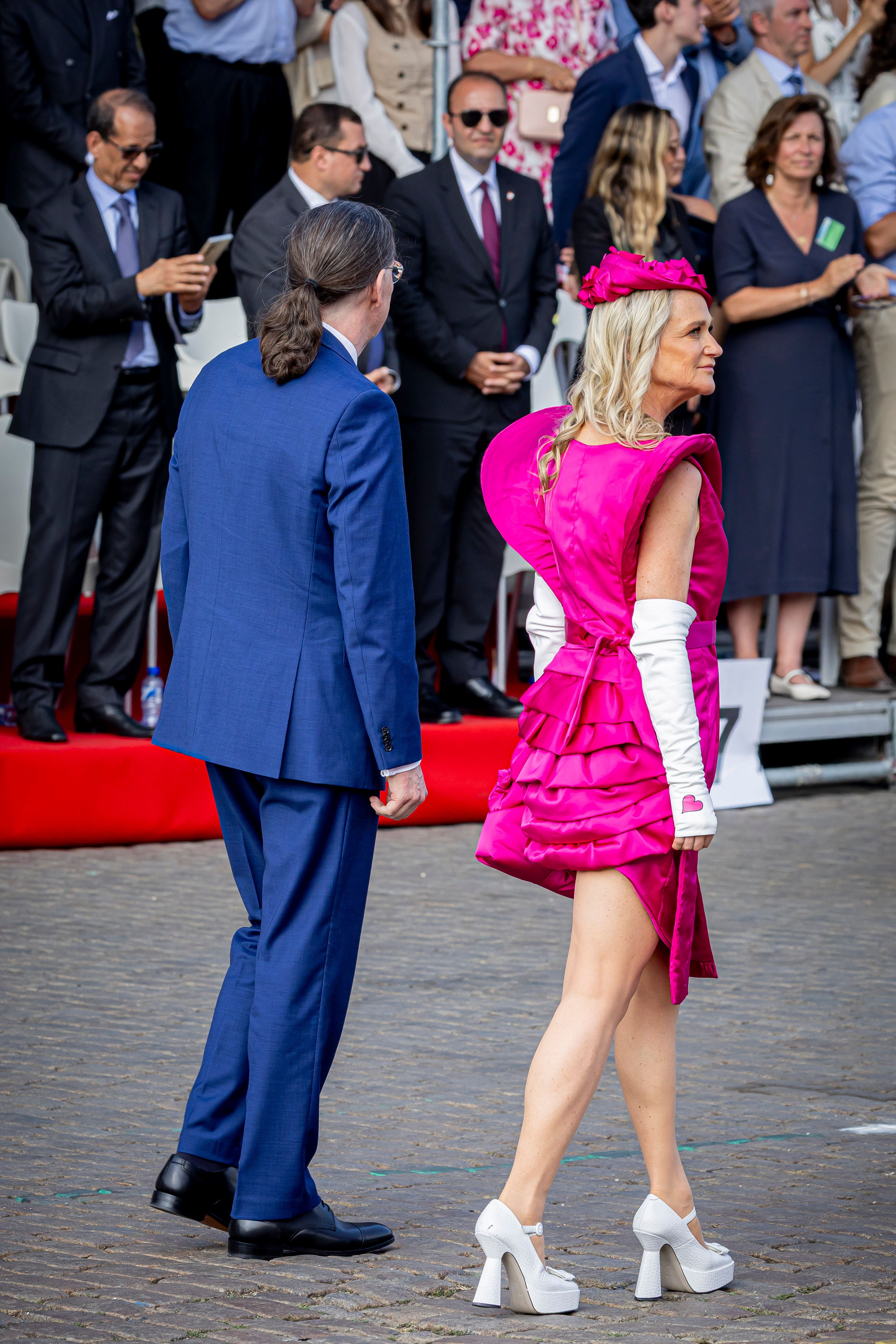 Eine Frau in pinkem Kleid und ein Mann im blauen Anzug laufen bei einer Parade.