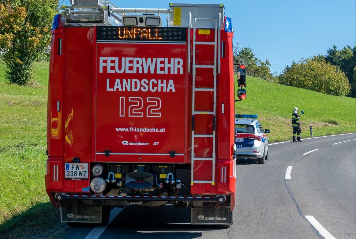 Feuerwehrauto und Polizeiwagen sichern Unfallstelle auf Landstraße, Einsatzkräfte vor Ort.