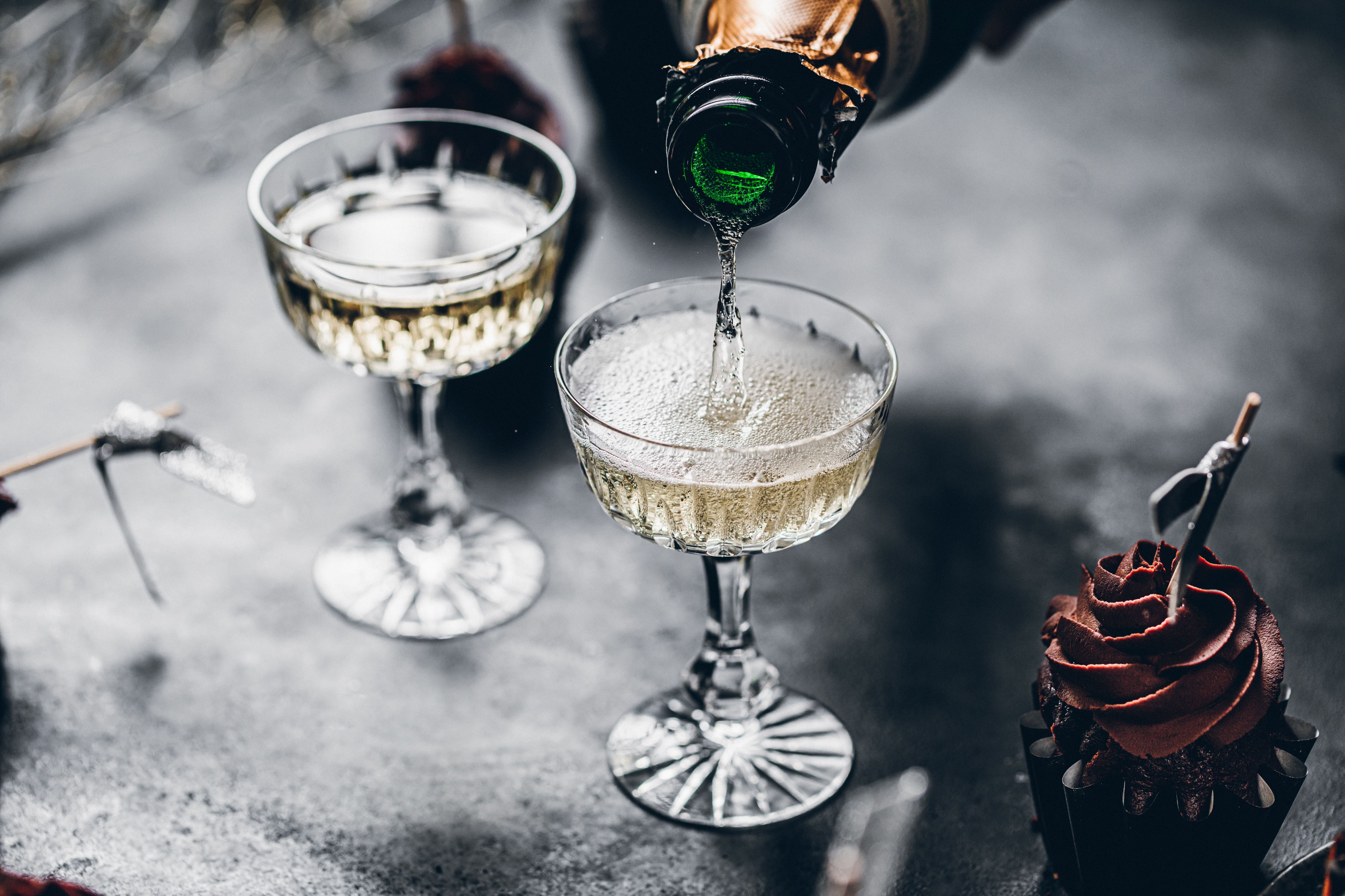 Champagner wird in Gläser gegossen, daneben ein Schokoladen-Cupcake auf dunklem Tisch.