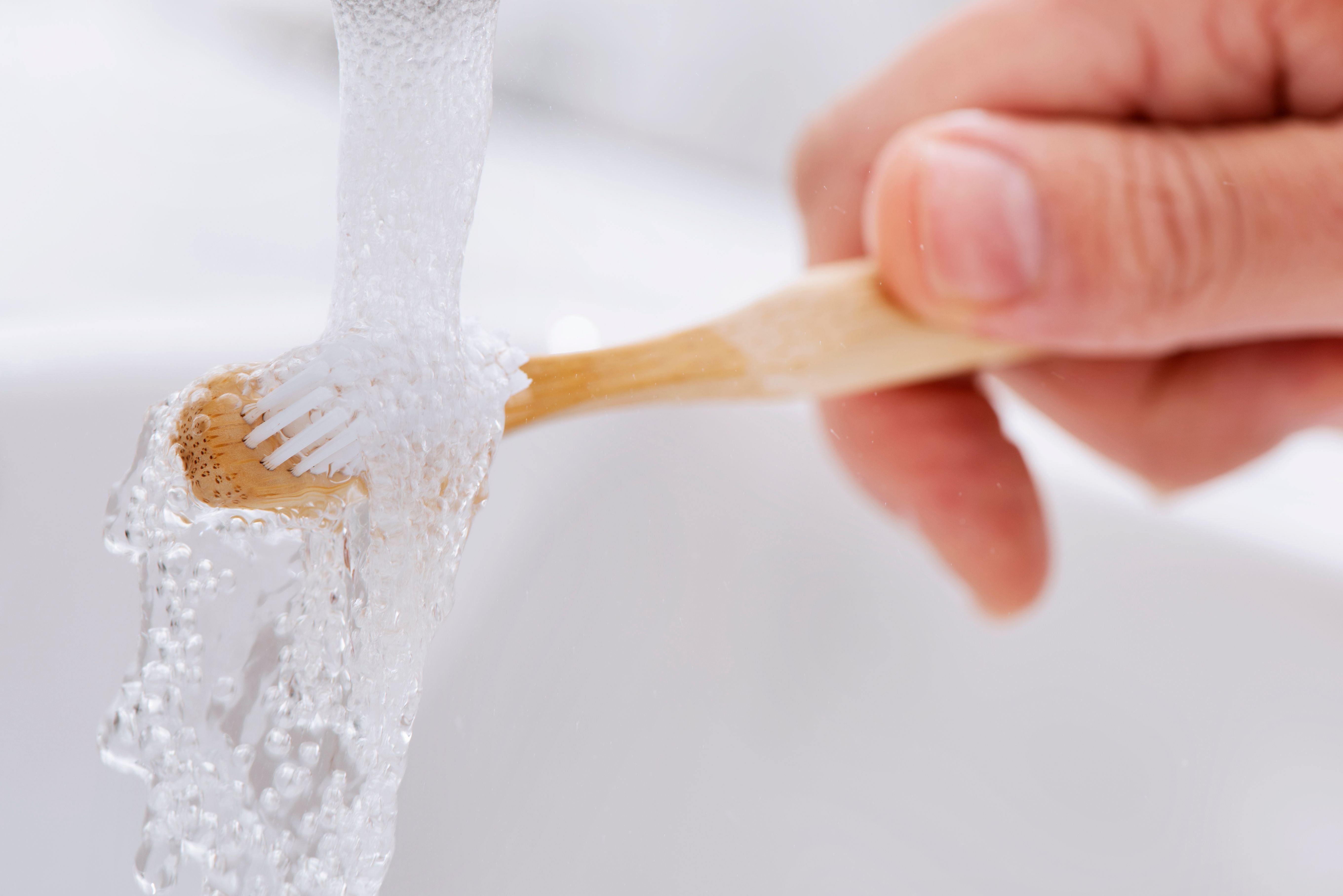 Nahaufnahme einer Bambuszahnbürste, die unter fließendem Wasser abgespült wird.
