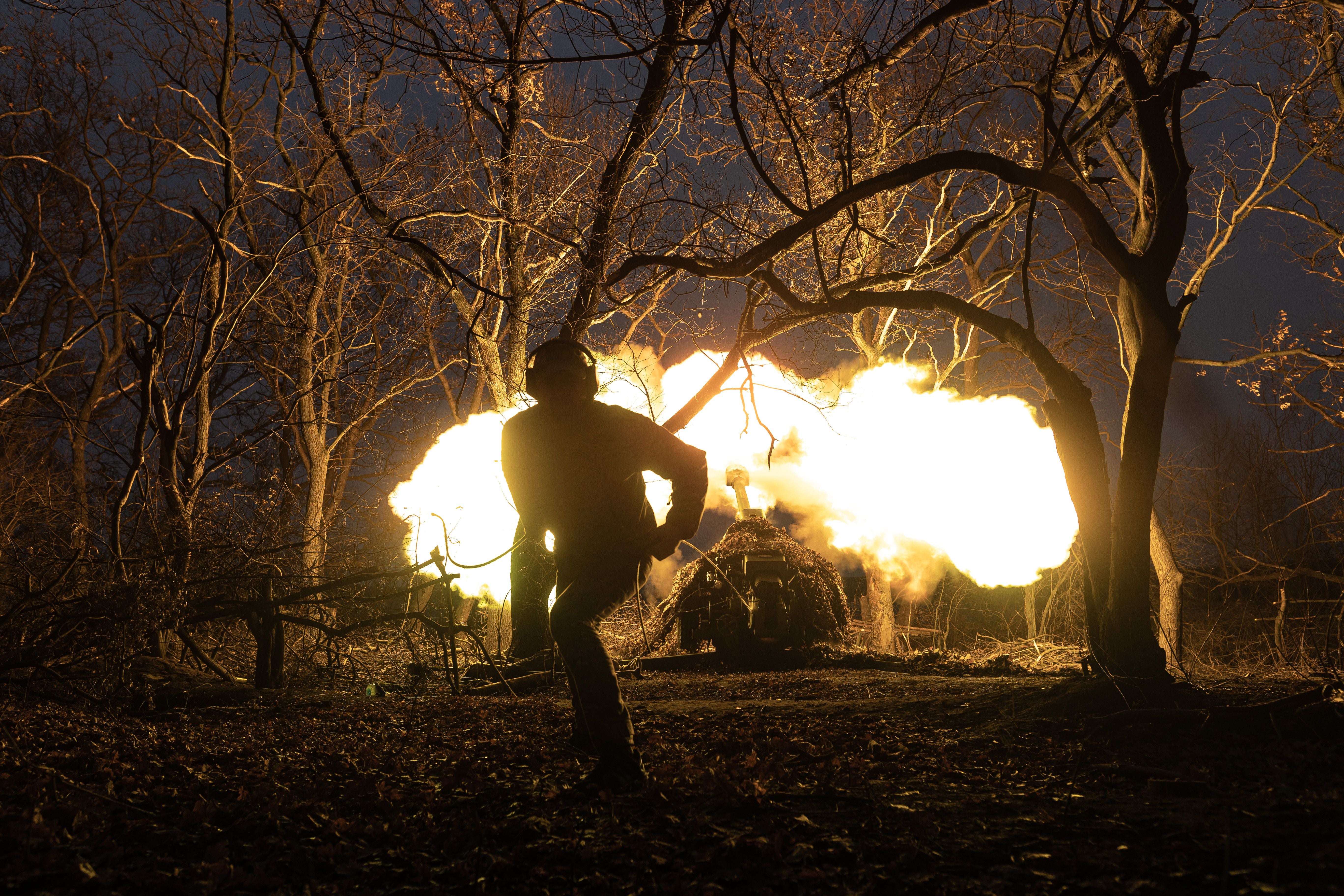 Ein Soldat feuert nachts im Wald eine D-30-Artillerie mit hellem Mündungsfeuer ab.