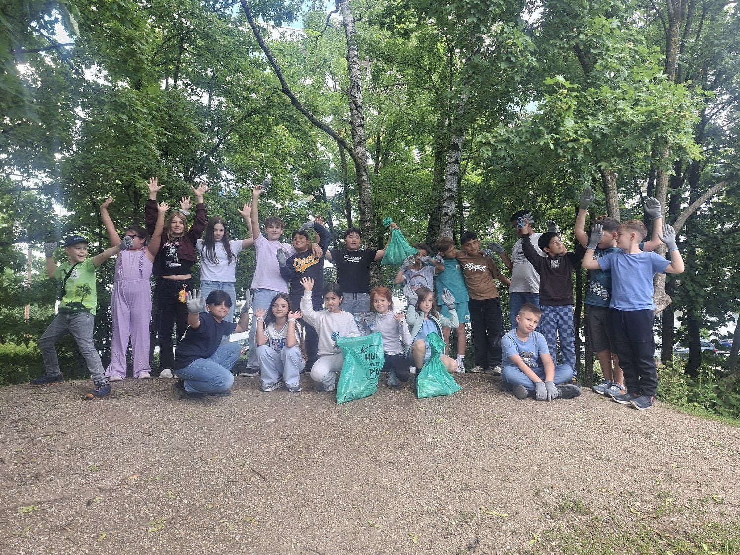 Eine Gruppe Kinder posiert mit Müllsäcken und Handschuhen im Grünen nach einer Aufräumaktion.