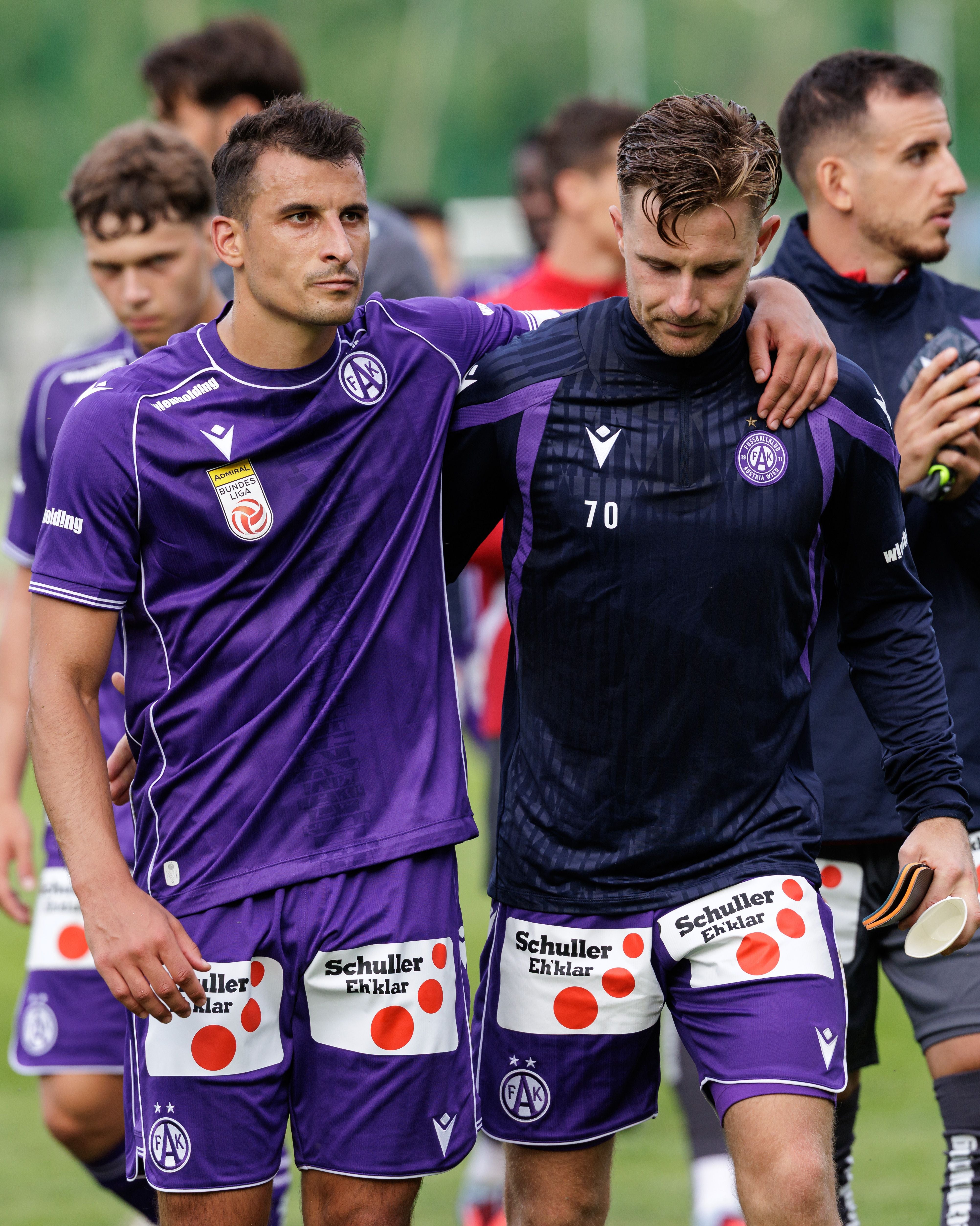 Zwei Fußballspieler von Austria Wien gehen Arm in Arm nach dem Spiel auf dem Spielfeld.