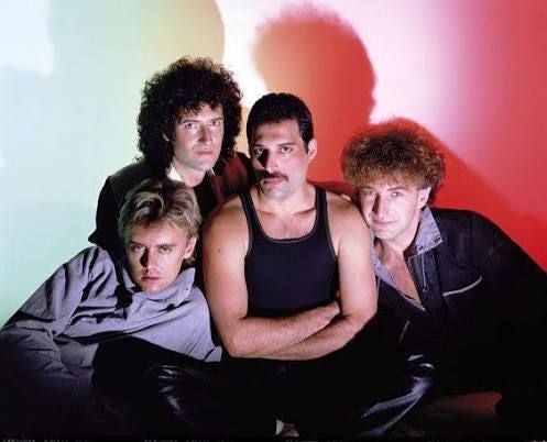 Vier Männer der Band Queen posieren vor einem rot-grünen Hintergrund.