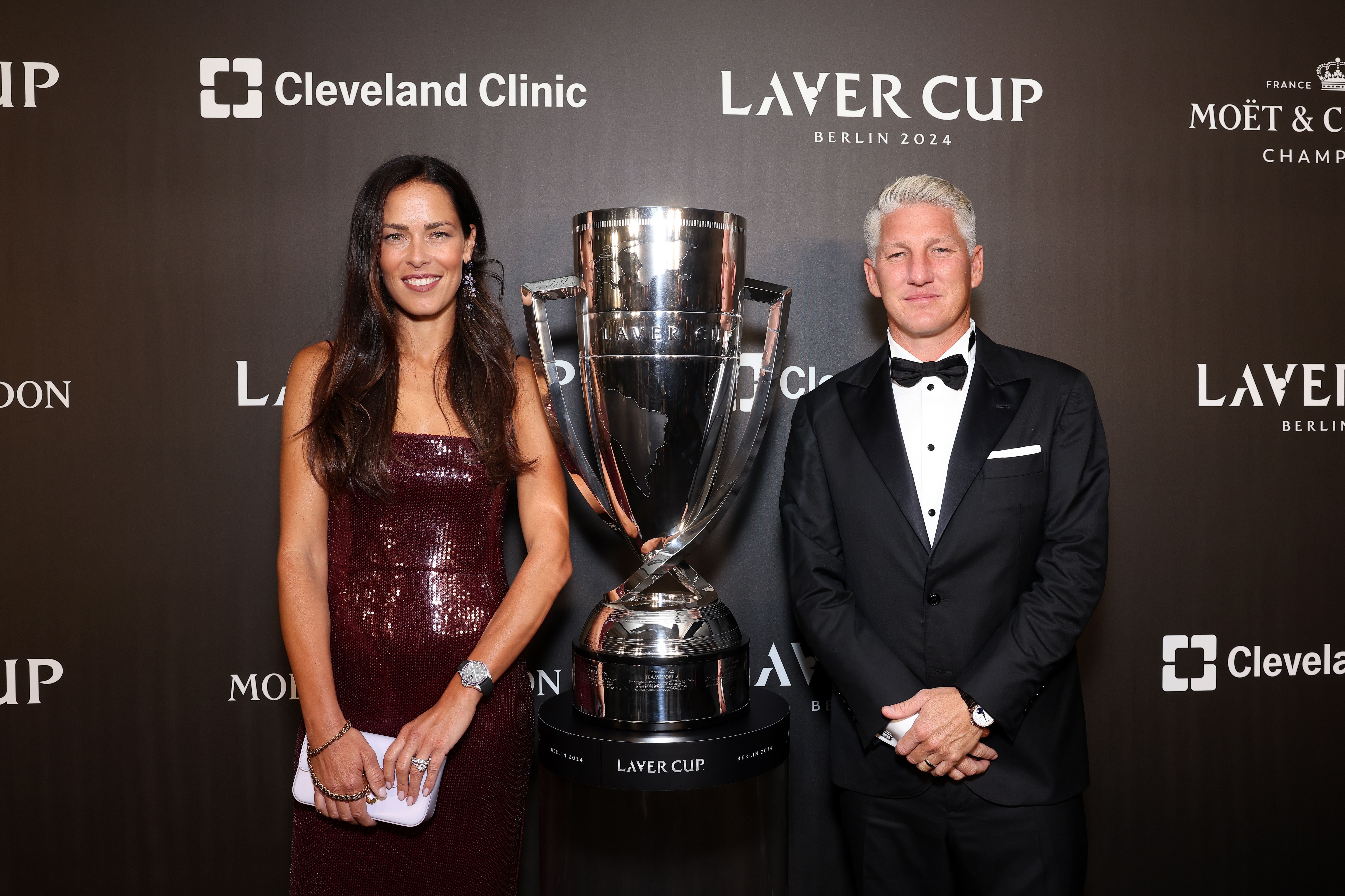 Eine Frau und ein Mann posieren elegant gekleidet neben einem großen Laver-Cup-Pokal.