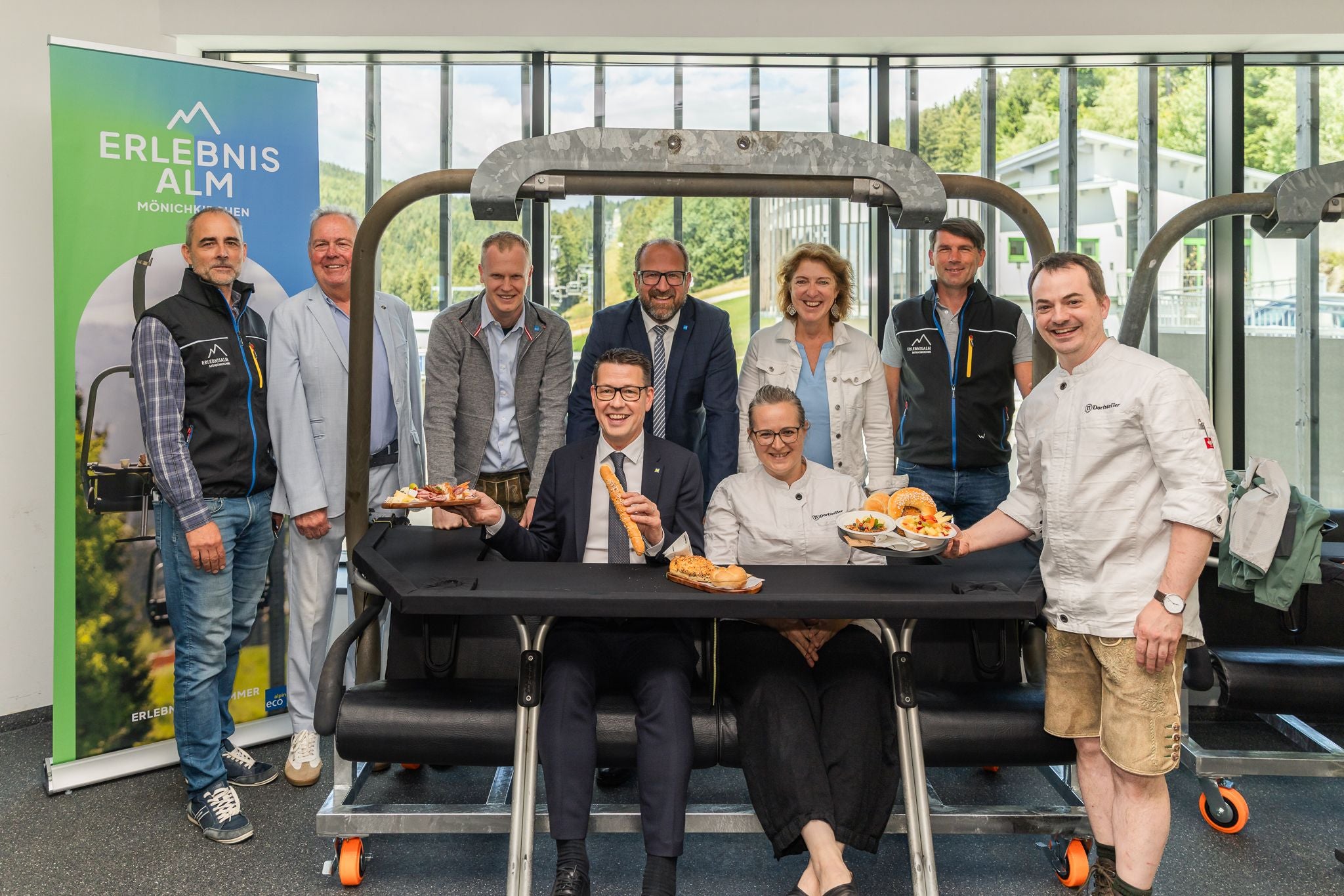 Gruppenfoto von neun Personen mit Speisen an einem Tisch in der Erlebnisalm Mönichkirchen.