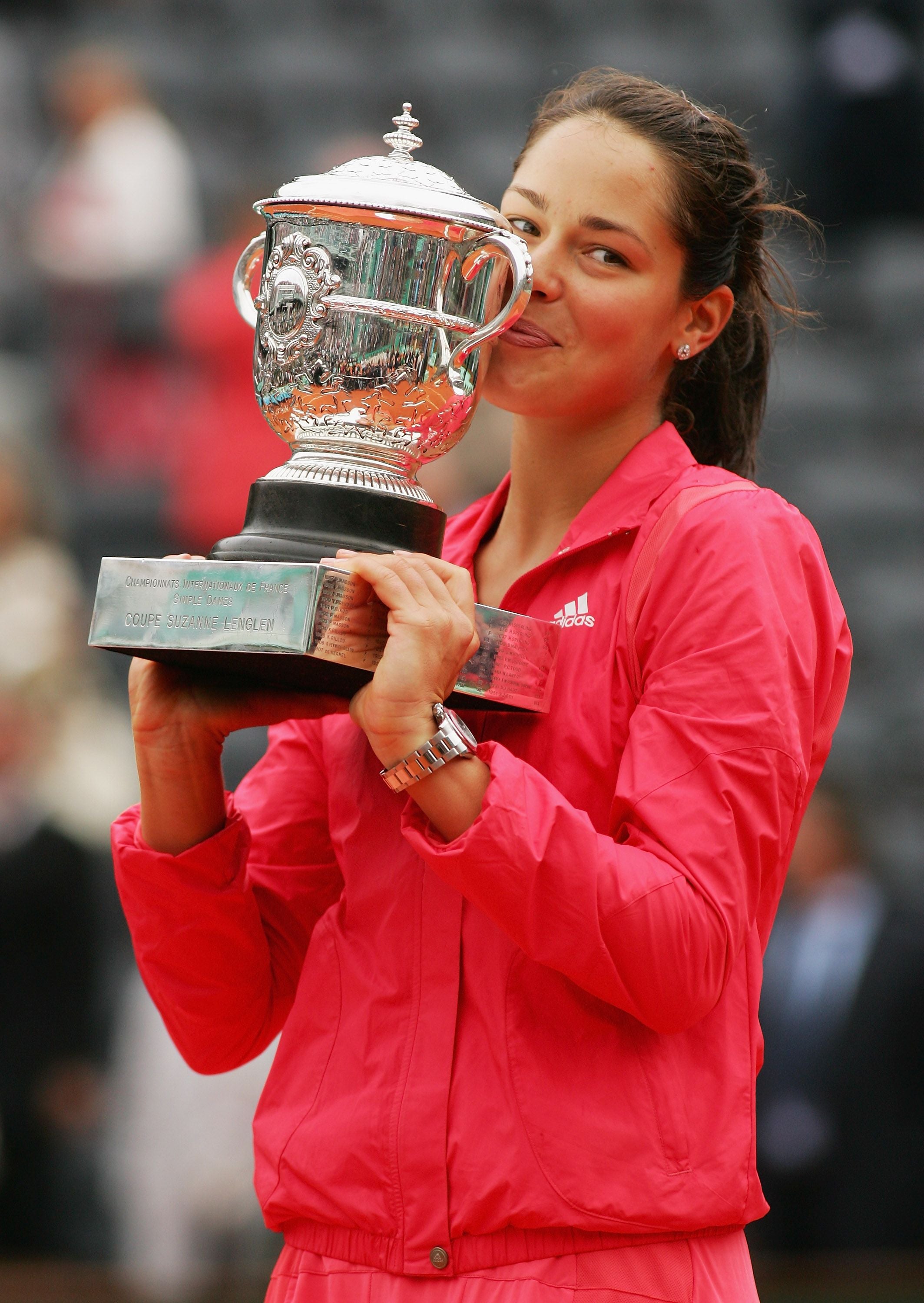 Tennisspielerin im pinken Outfit küsst den silbernen French-Open-Pokal auf dem Tennisplatz.