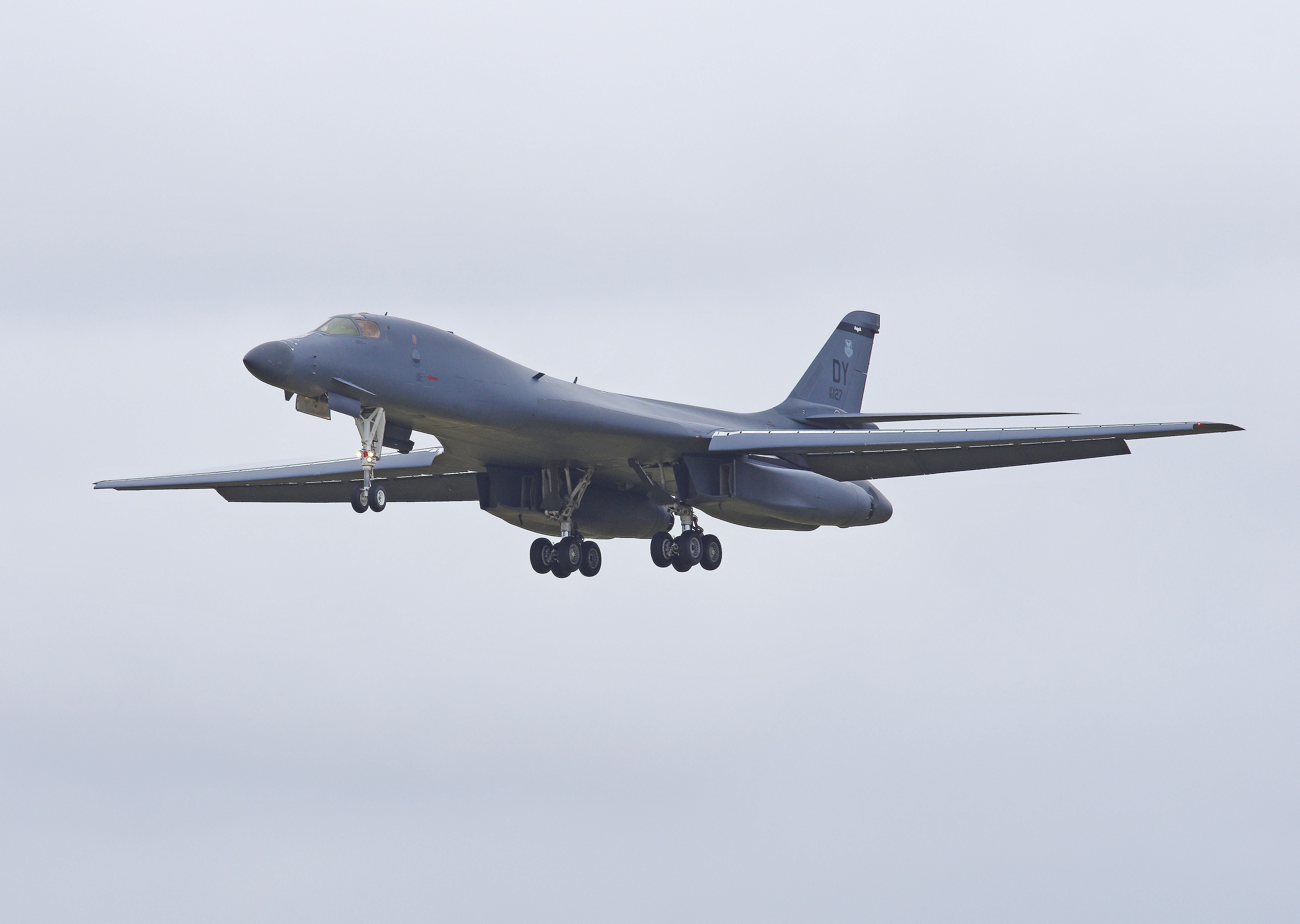 Ein Rockwell B-1 Lancer Bomber landet mit ausgefahrenem Fahrwerk bei bewölktem Himmel.