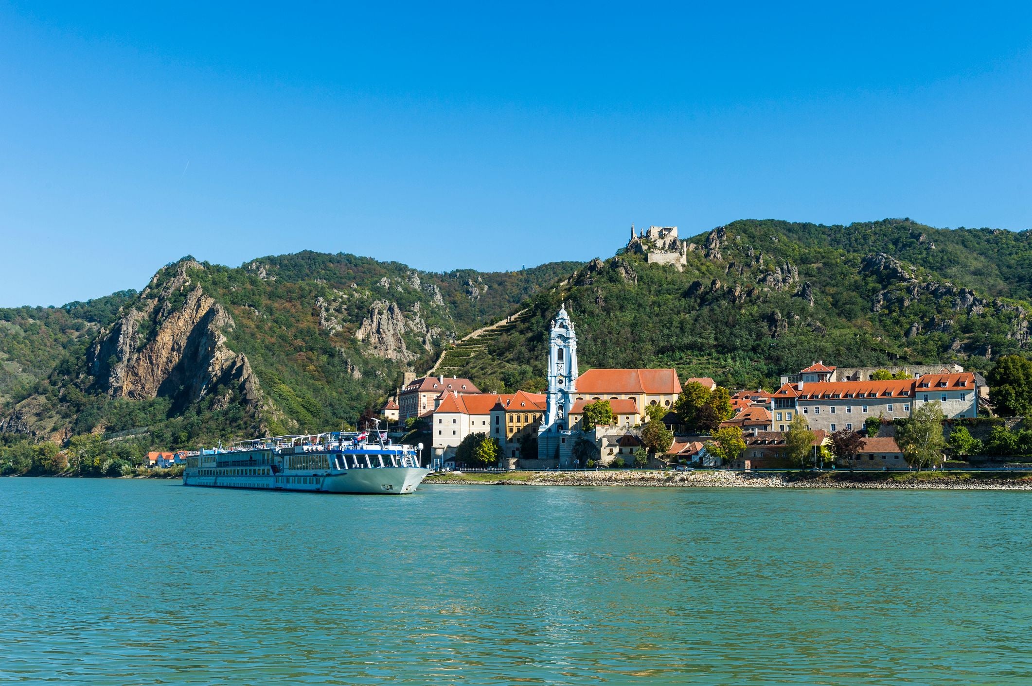 Ein Kreuzfahrtschiff fährt auf der Donau an Dürnstein mit Kirche und Ruine vorbei.