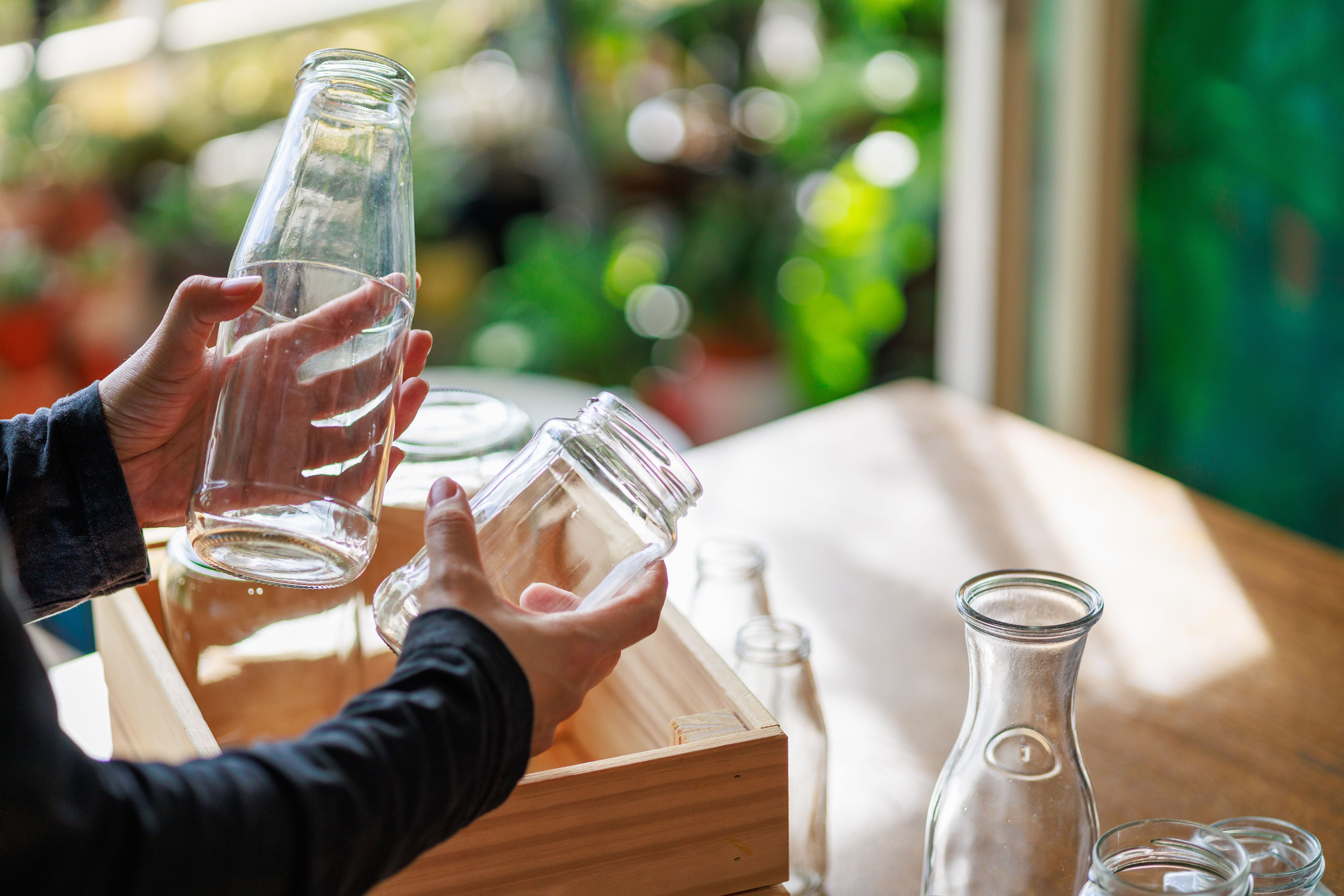 Hände stellen leere Glasflaschen zur Wiederverwertung in eine Holzkiste auf einem Tisch.