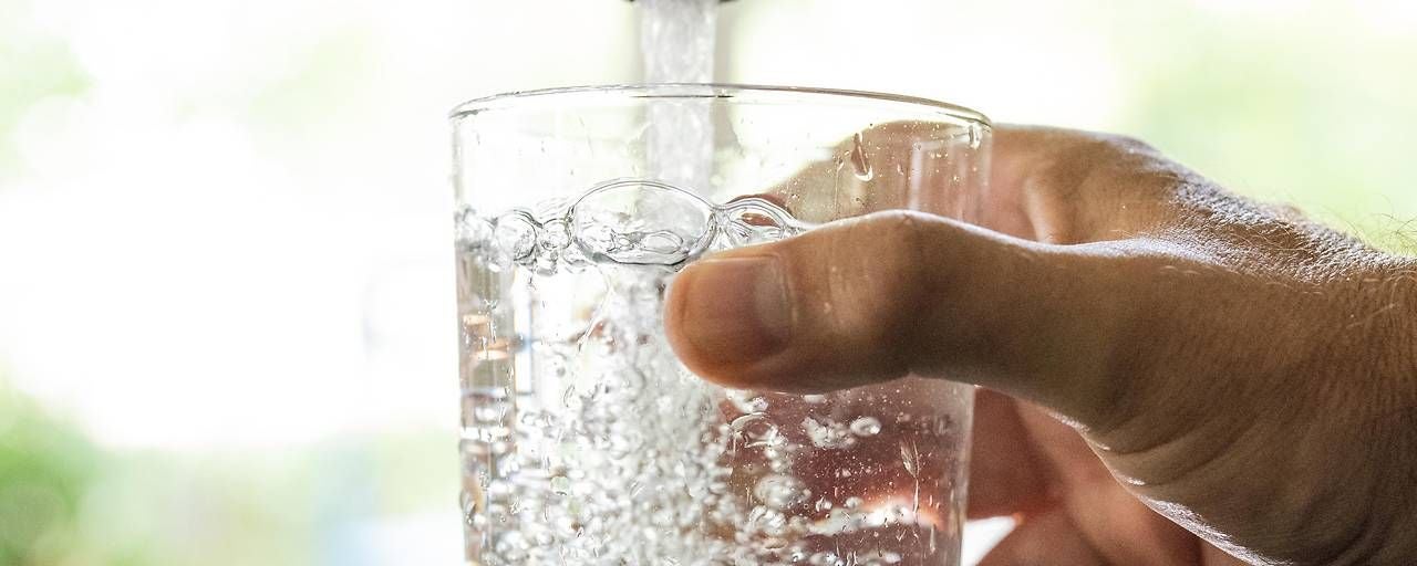 Ein Glas wird unter einem Wasserhahn mit Leitungswasser gefüllt.