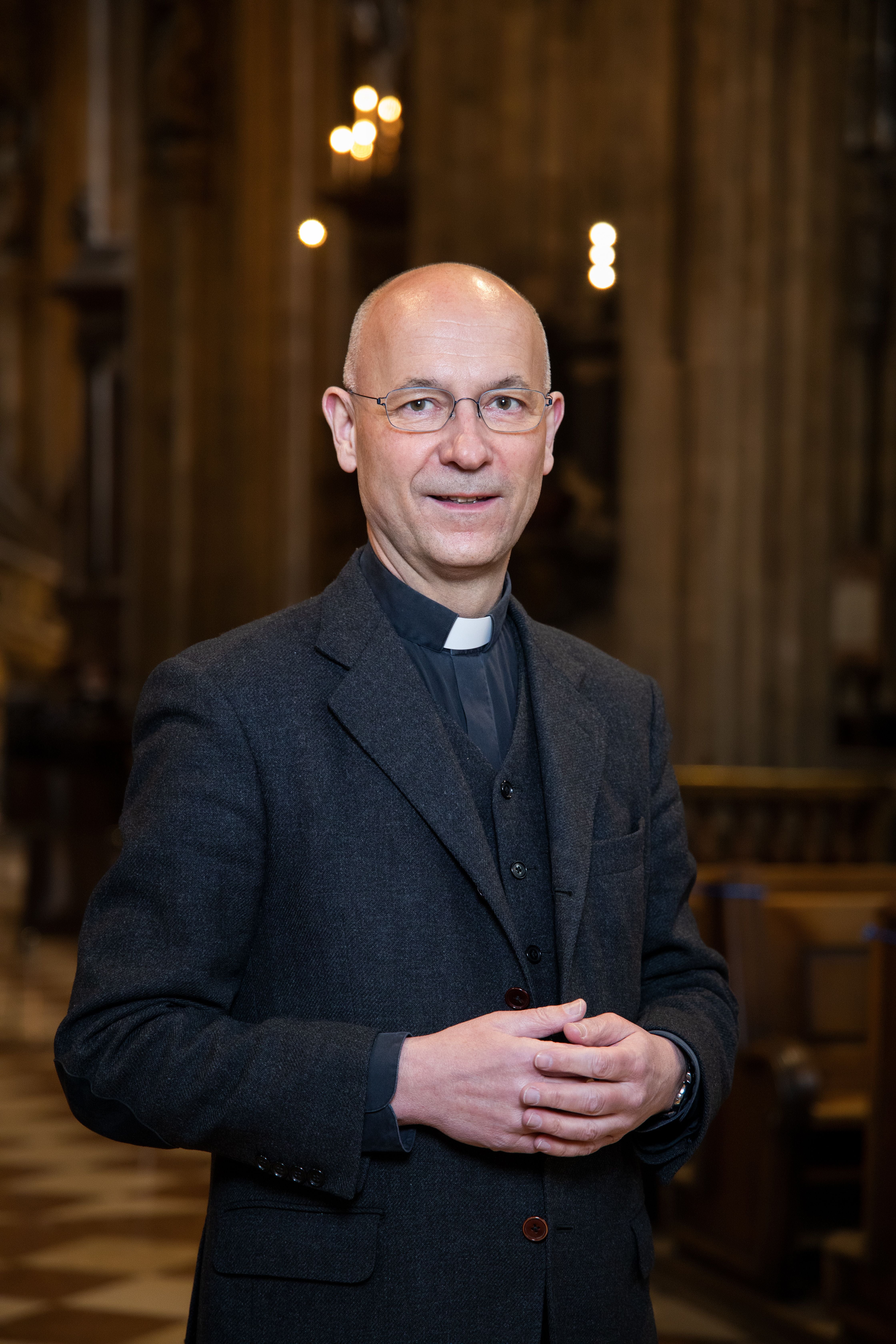 Ein Geistlicher mit Brille steht in einer Kirche und blickt freundlich in die Kamera.