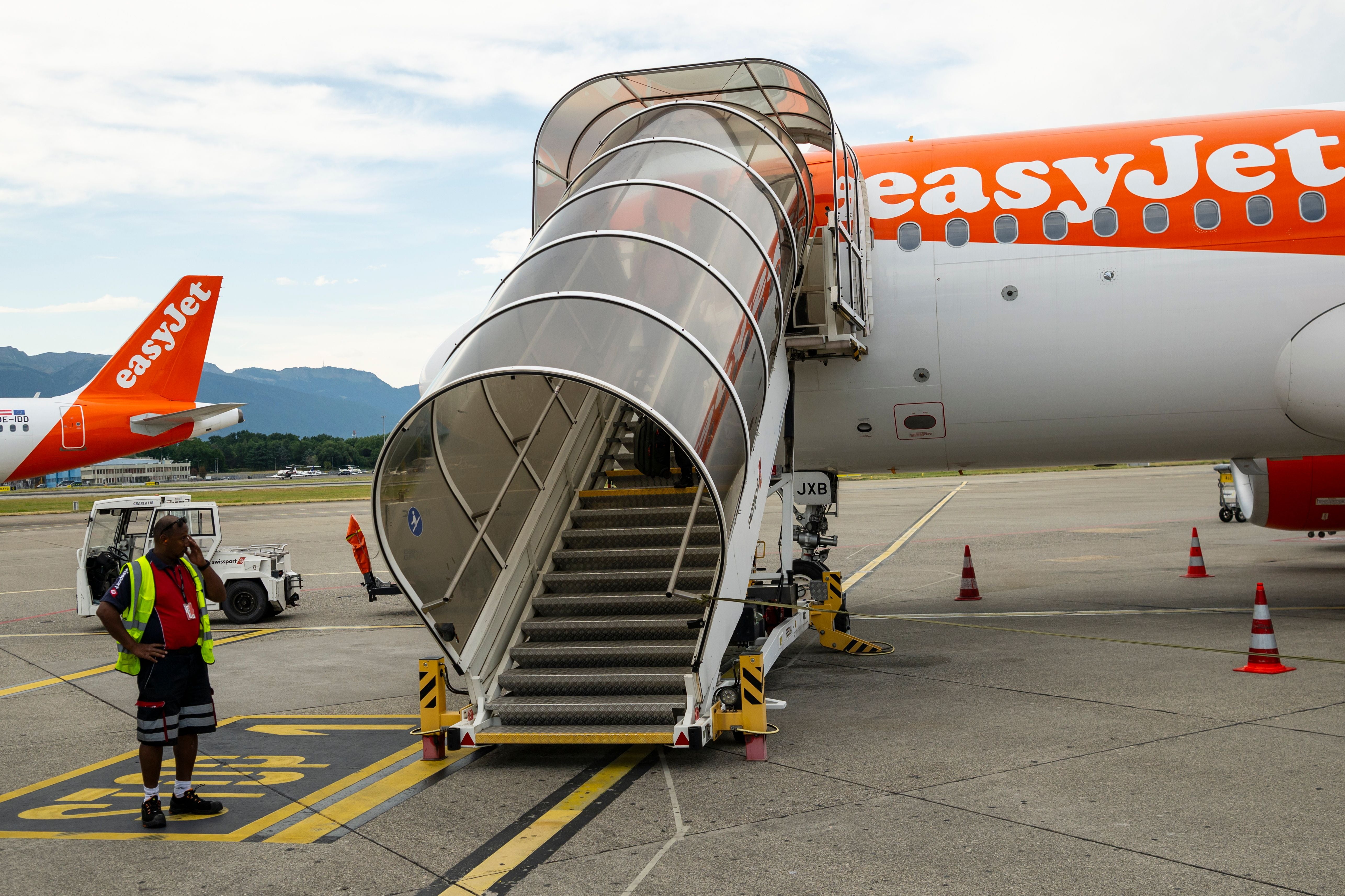 Ein easyJet-Flugzeug steht am Flughafen Genf mit offener Fluggasttreppe und Bodenpersonal.