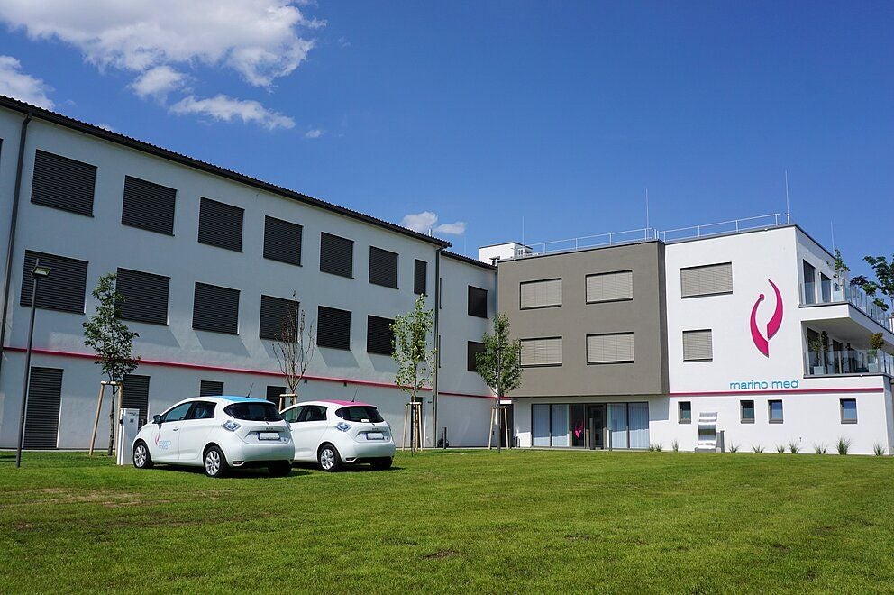 Modernes Firmengebäude von Marinomed Biotech AG mit zwei weißen Autos davor und grüner Rasenfläche.