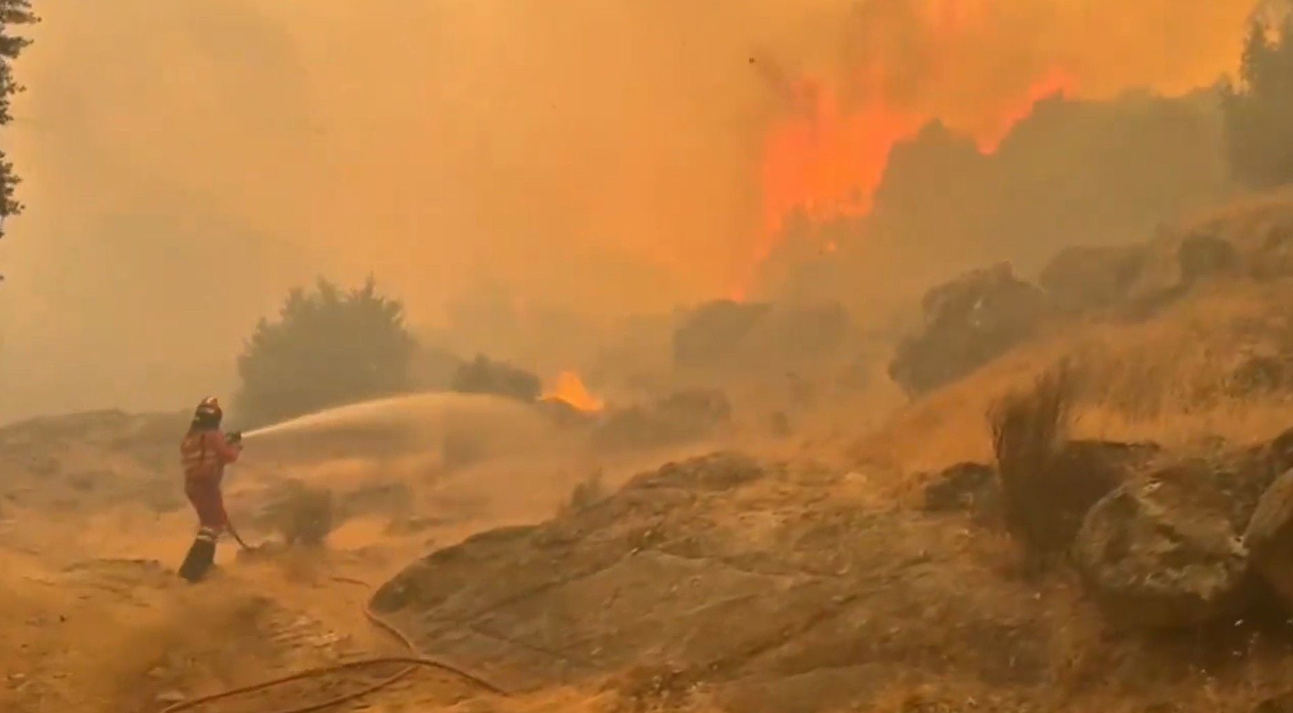 Feuerwehrmann bekämpft großen Waldbrand in einer bergigen, rauchigen Landschaft.
