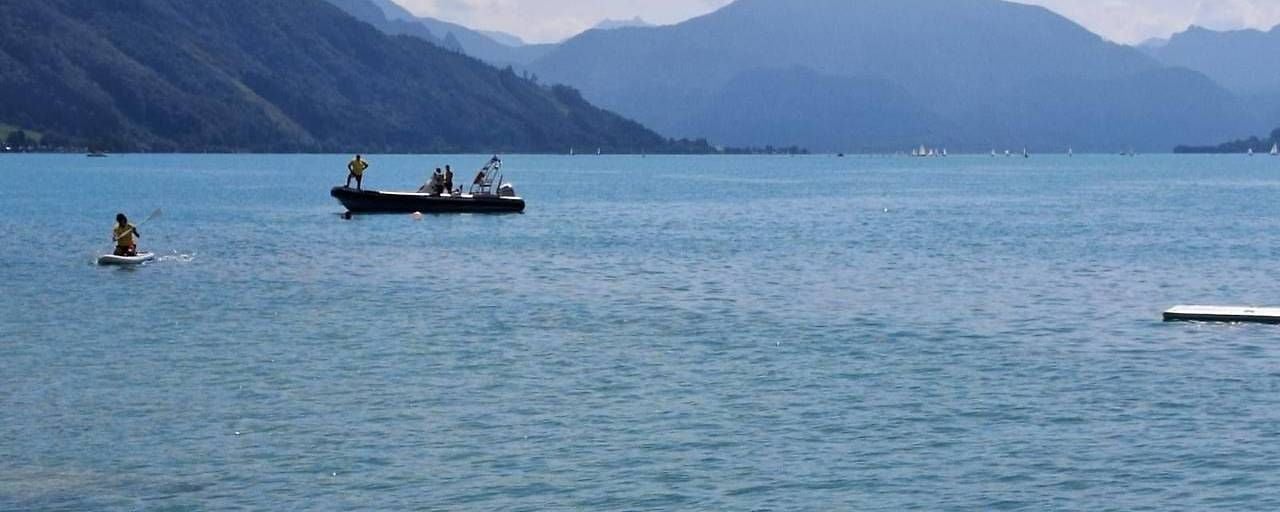 Menschen fahren bei bewölktem Wetter mit Boot und SUP auf einem See in den Bergen.
