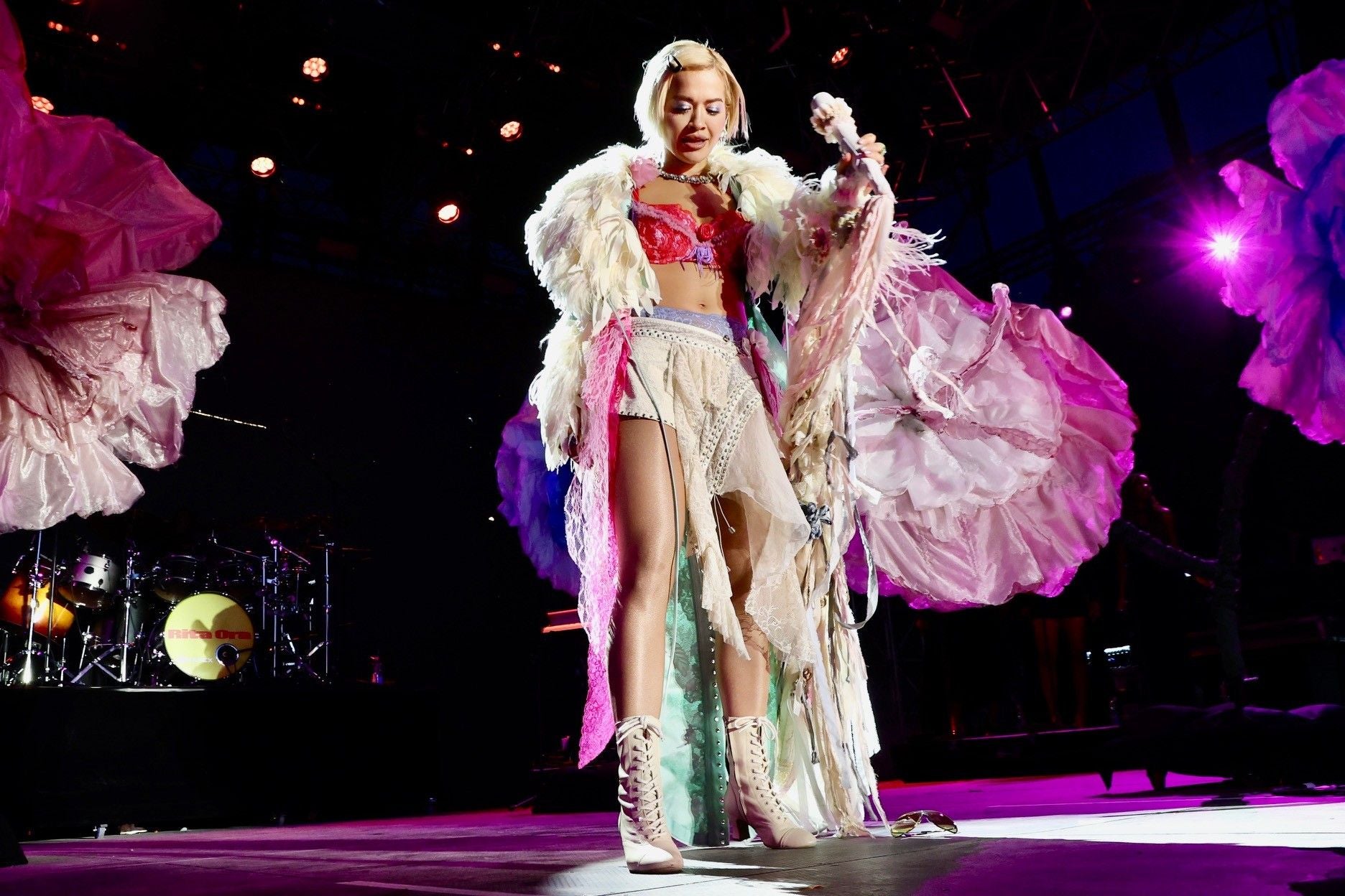 Rita Ora tritt in auffälligem Bühnenoutfit auf einer bunt beleuchteten Bühne auf.