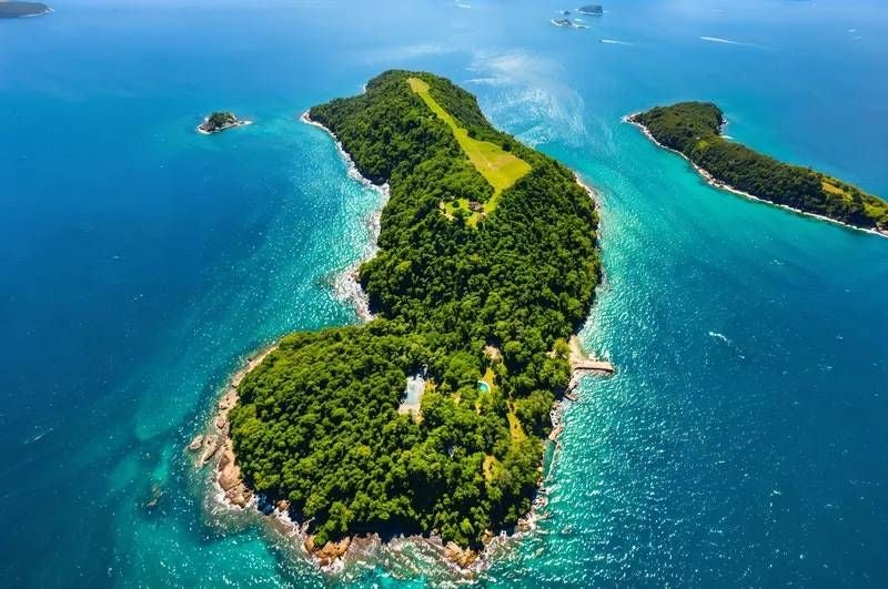 Luftaufnahme einer grünen Luxus-Insel im türkisblauen Meer mit weiteren kleinen Inseln in der Nähe.