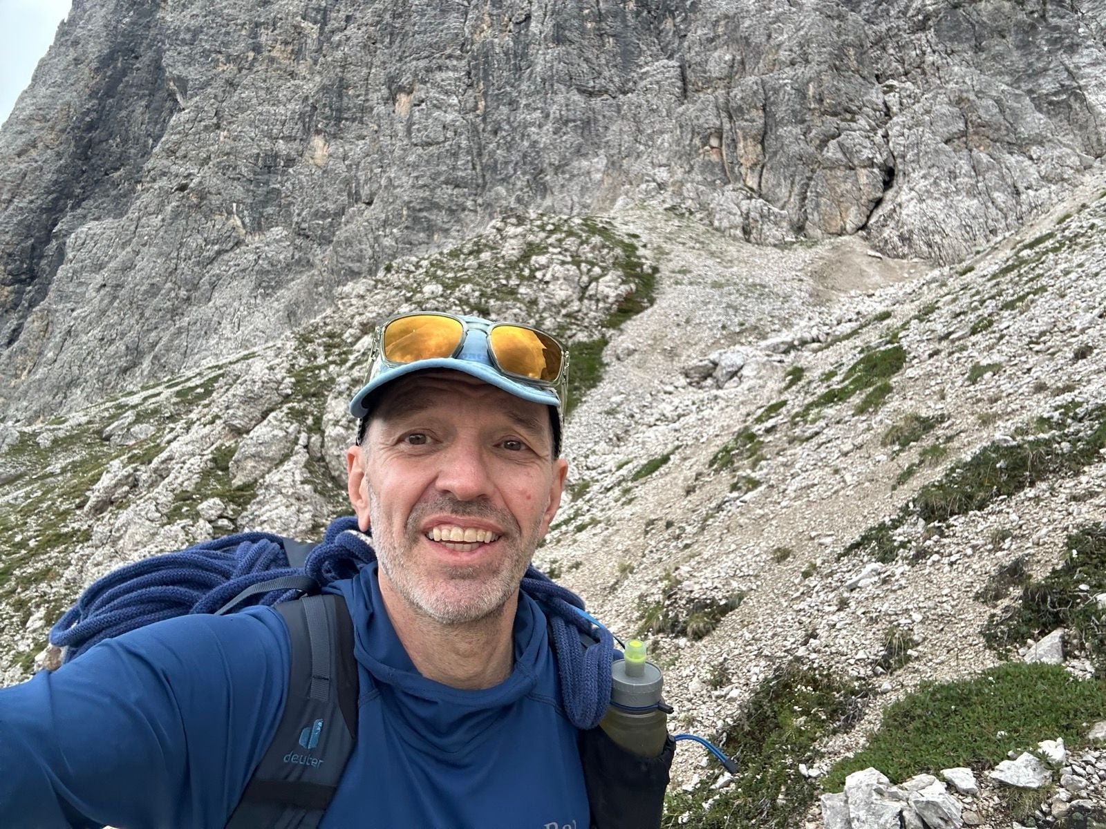 Ein Mann macht ein Selfie beim Wandern vor einer felsigen Berglandschaft.