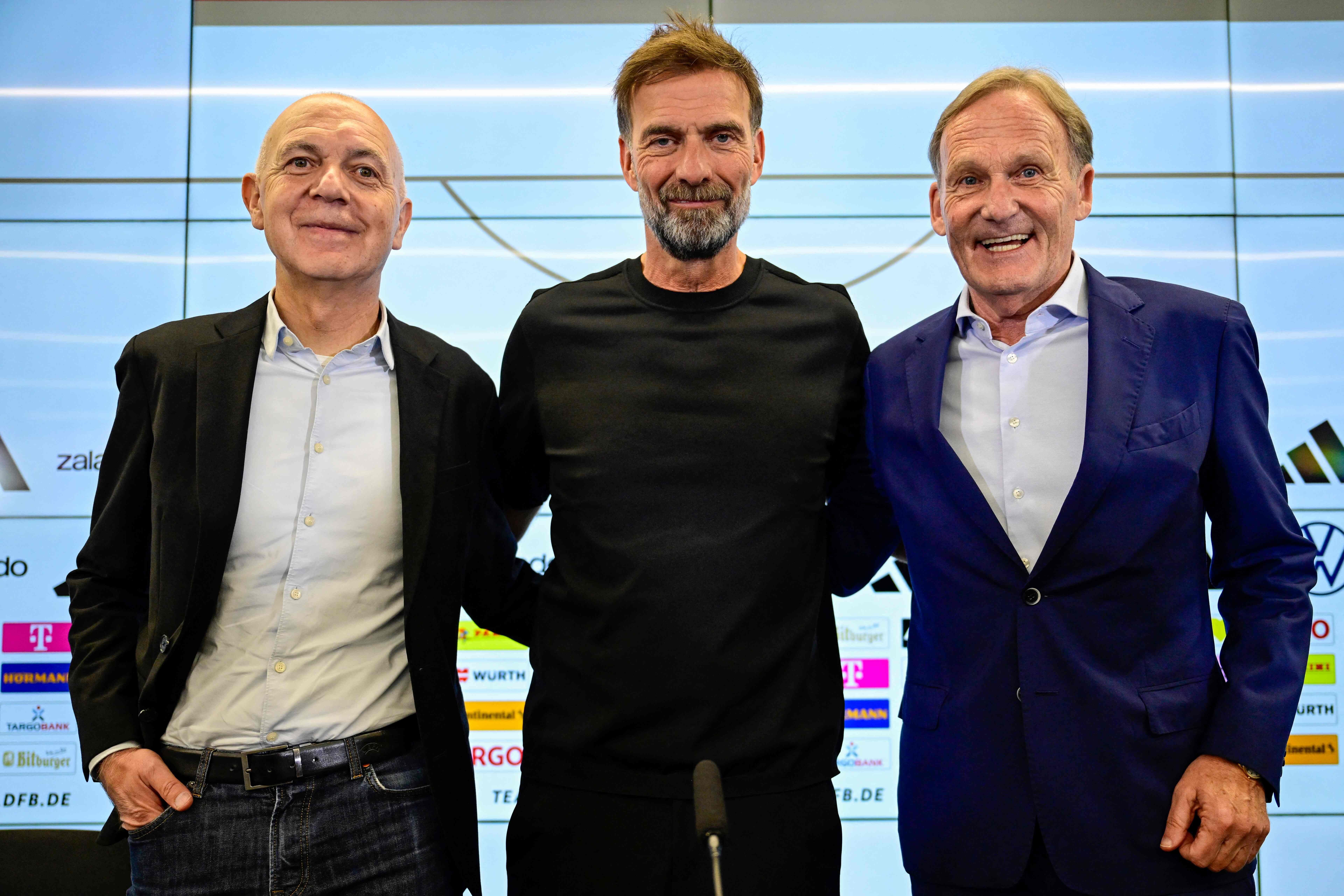 Drei Männer posieren lächelnd zusammen bei einer Pressekonferenz vor Sponsorenlogos.