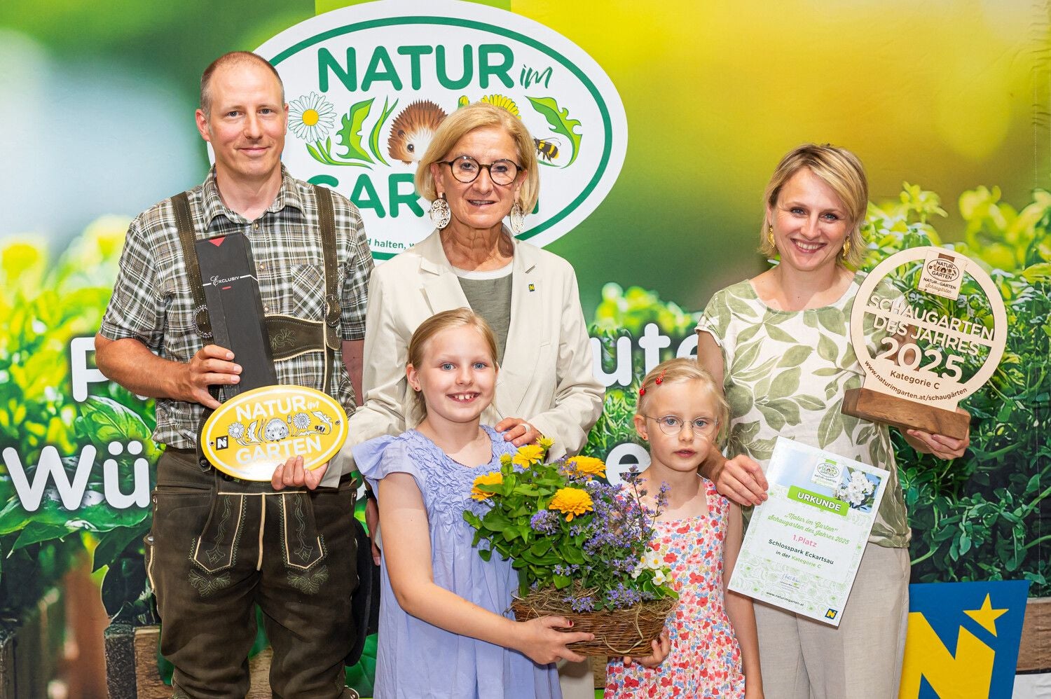 Eine Familie mit Auszeichnungen steht vor einem "Natur im Garten"-Plakat und lächelt in die Kamera.