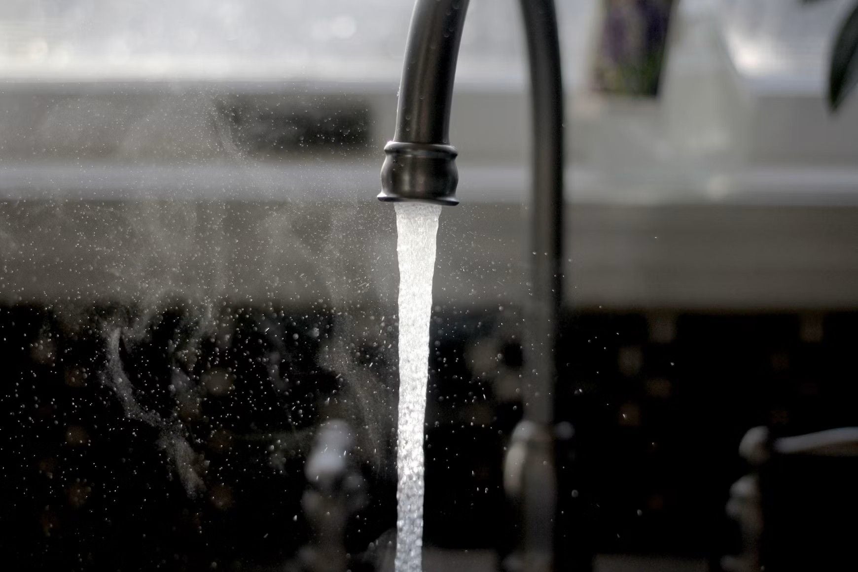 Ein Wasserhahn mit fließendem Wasser in einer Küche, Tageslicht im Hintergrund.
