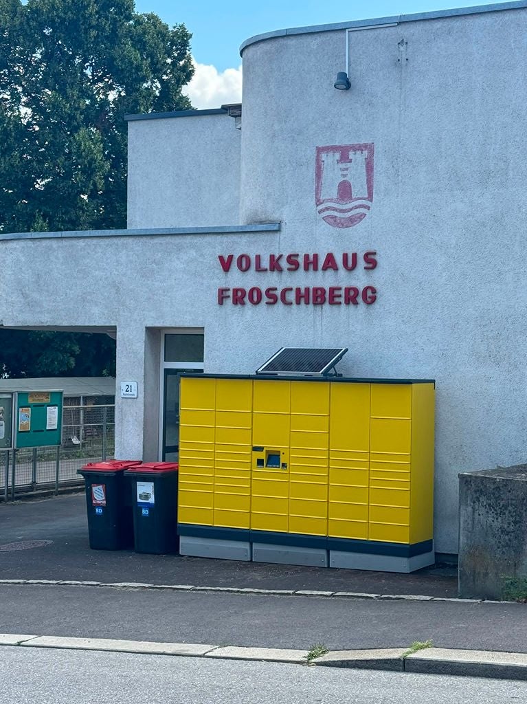 Gelbe Post-Selbstbedienungsstation vor dem Volkshaus Froschberg in Linz.