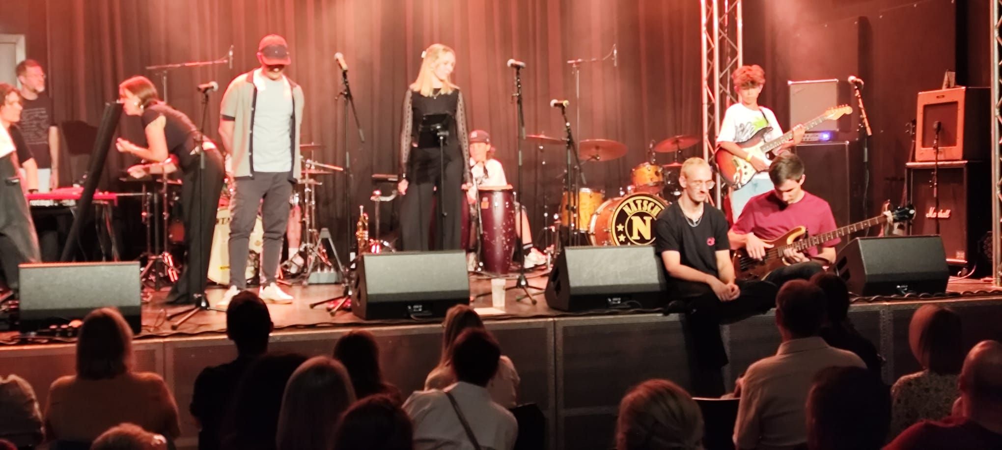 Jugendliche spielen auf einer Bühne in einer Band, das Publikum sitzt davor.