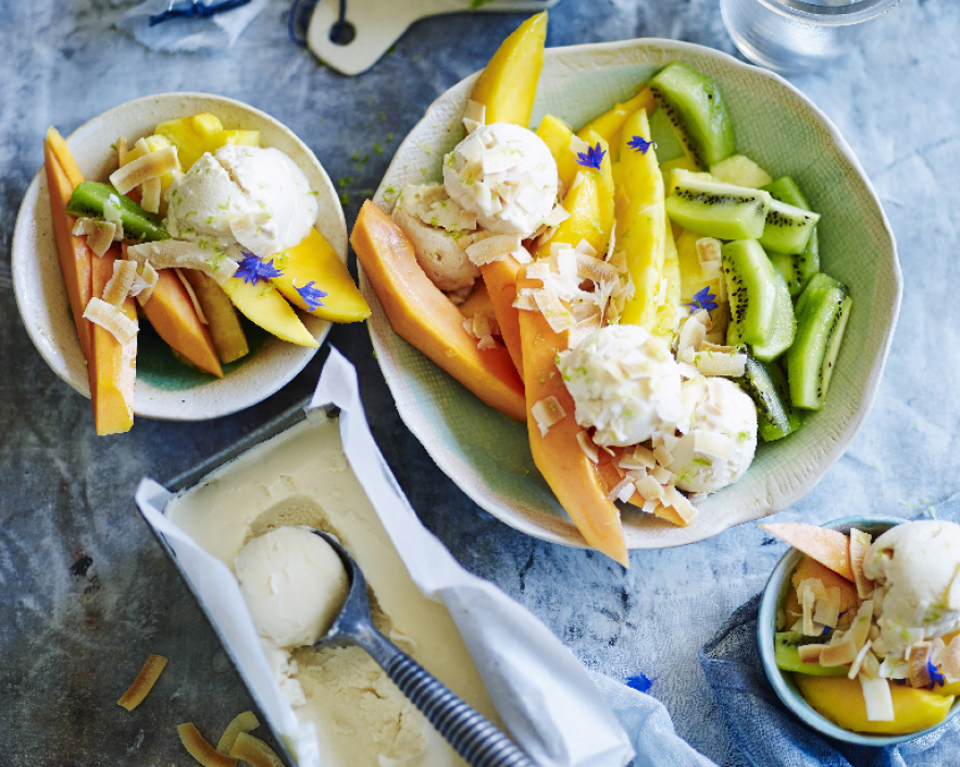 Schalen mit Vanilleeis, Melone, Mango, Kiwi, gerösteten Kokoschips und essbaren Blüten.