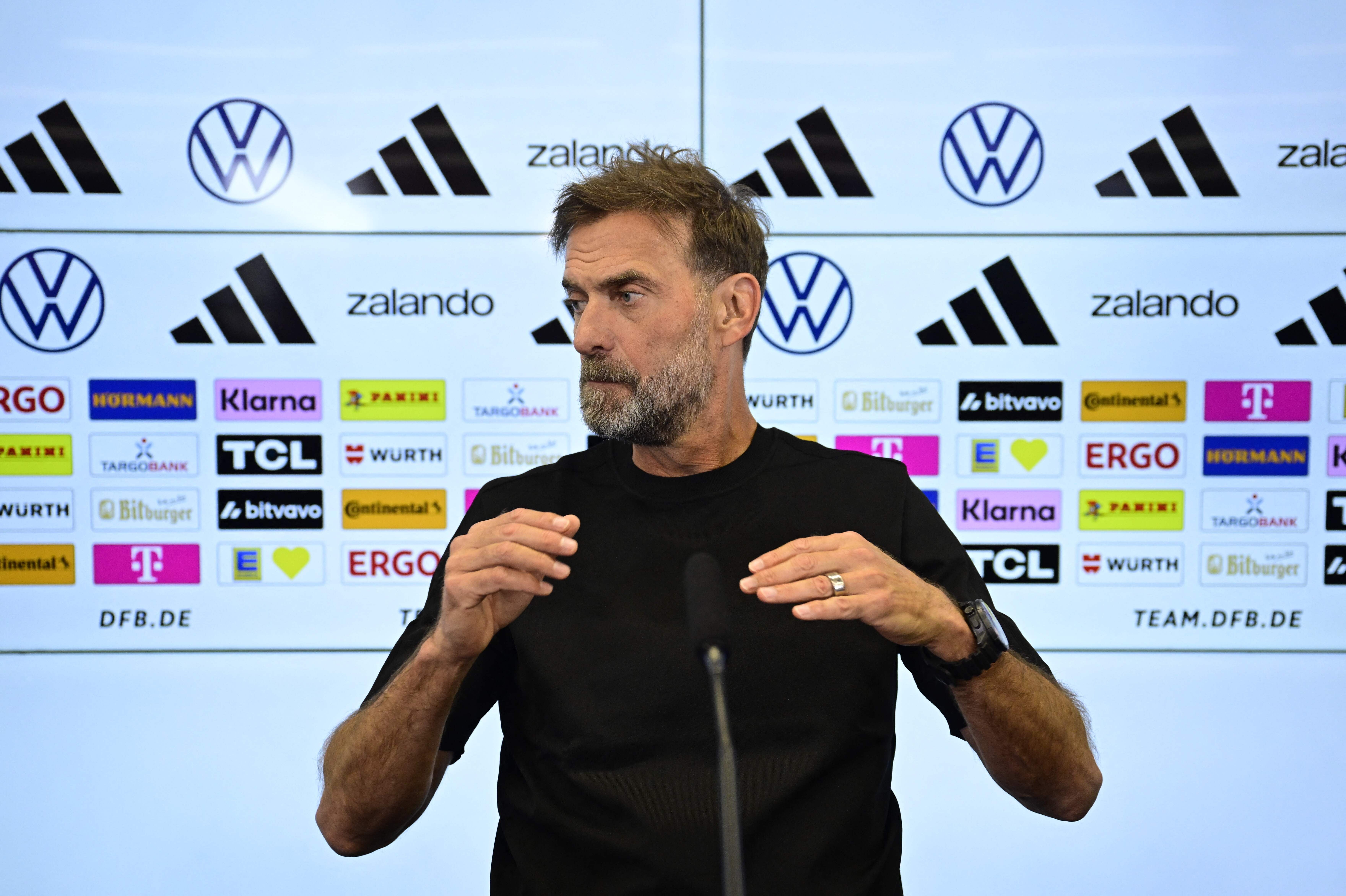 Ein Mann spricht auf einer Pressekonferenz vor Werbewänden mit Logos und Sponsoren.