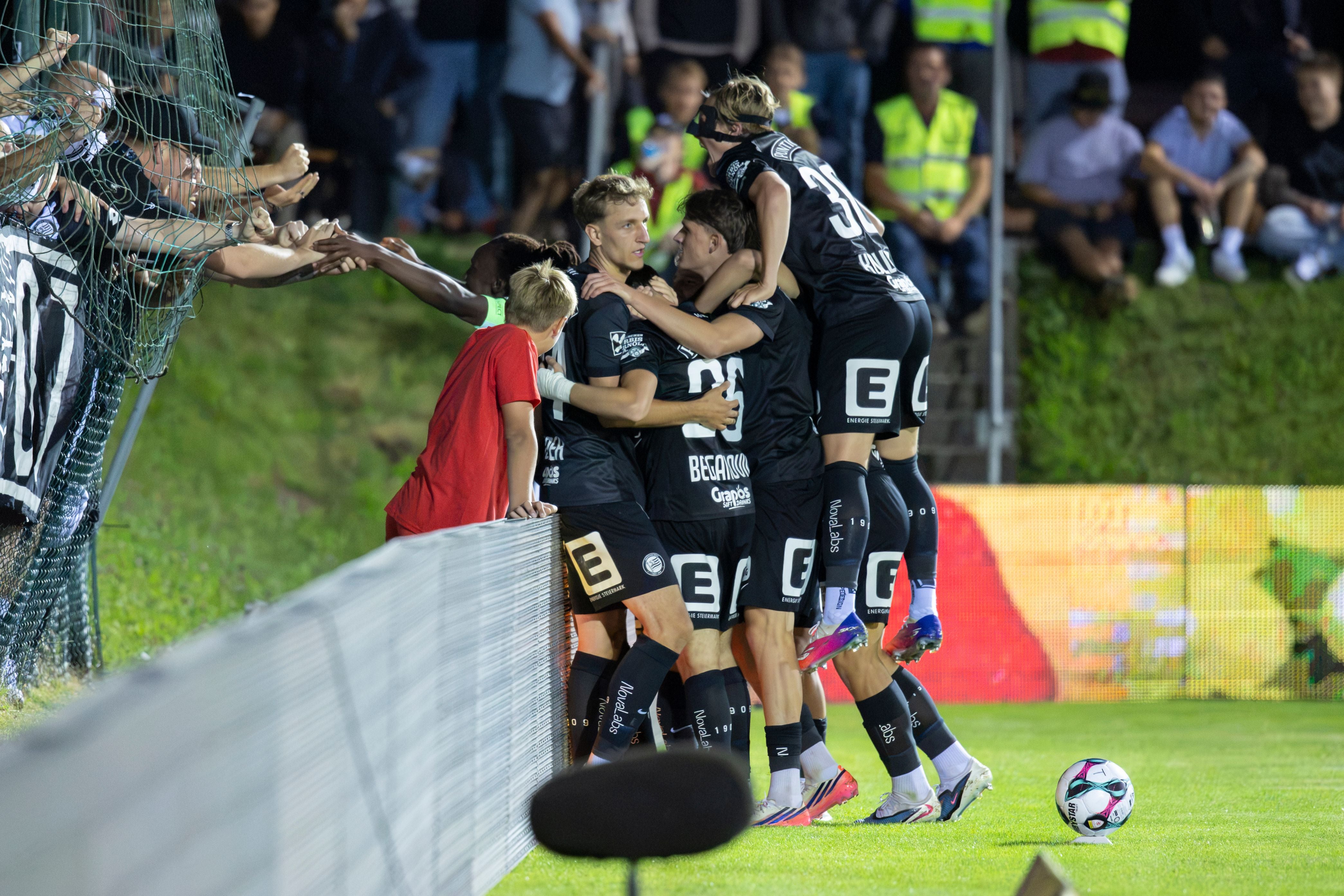 Fußballspieler von SK Sturm Graz feiern ein Tor mit Fans am Spielfeldrand.