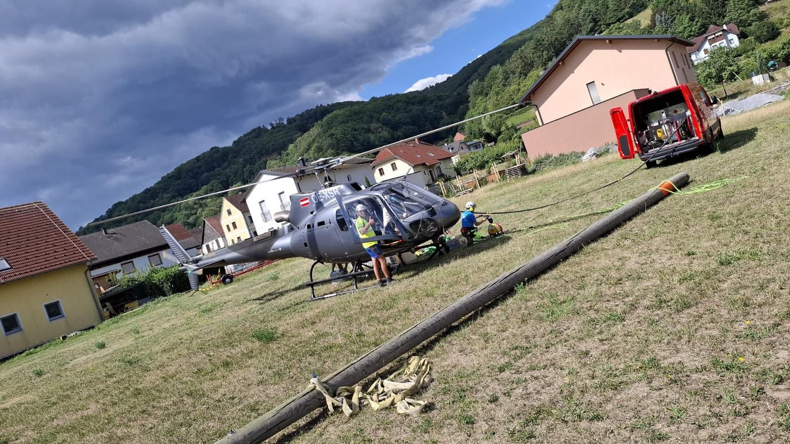 Ein Hubschrauber und Arbeiter bereiten einen Strommast im Garten eines Wohngebiets vor.