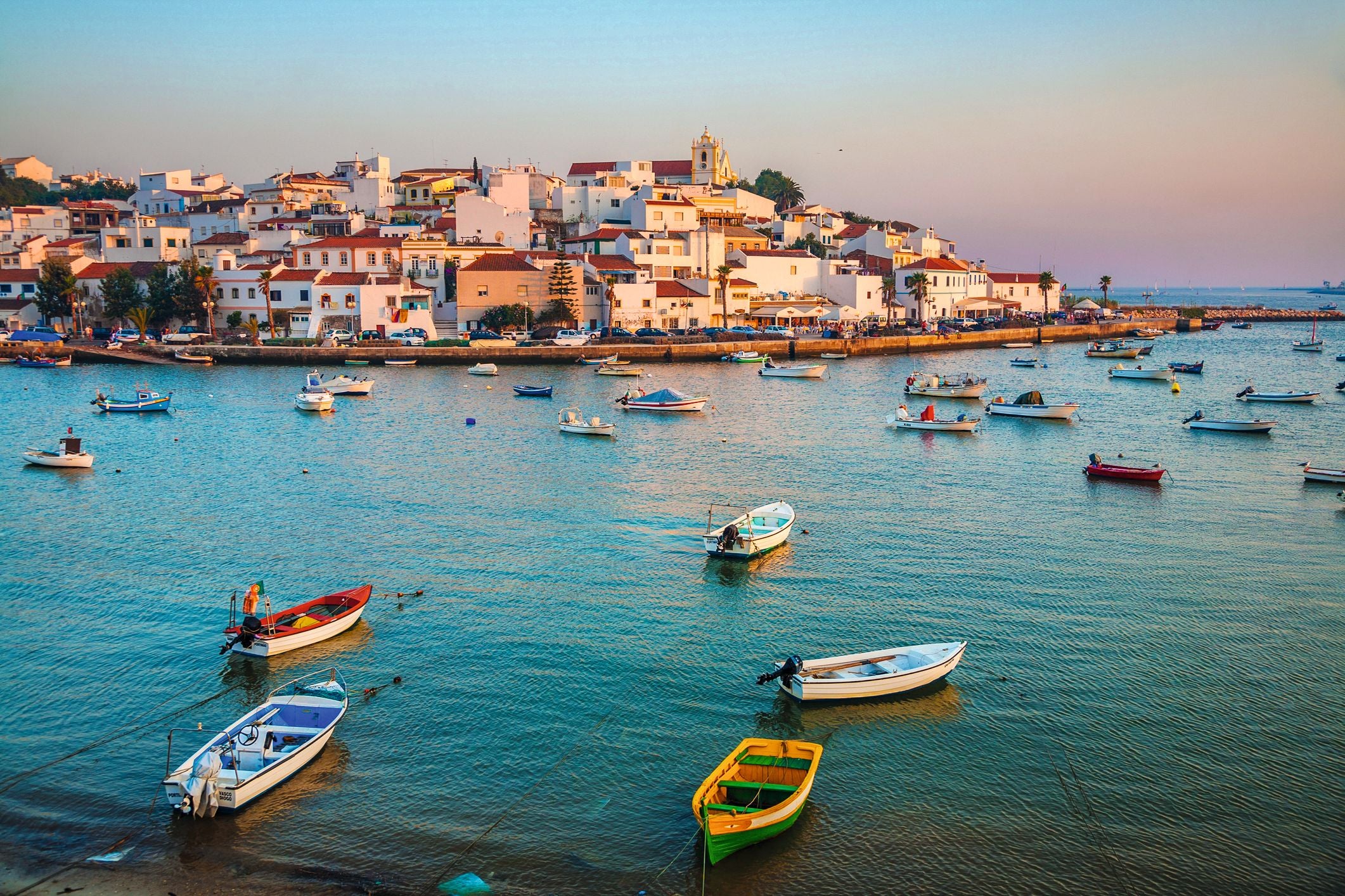 Bunte Boote schwimmen vor weißen Häusern an der Küste von Ferragudo in der Algarve, Portugal.