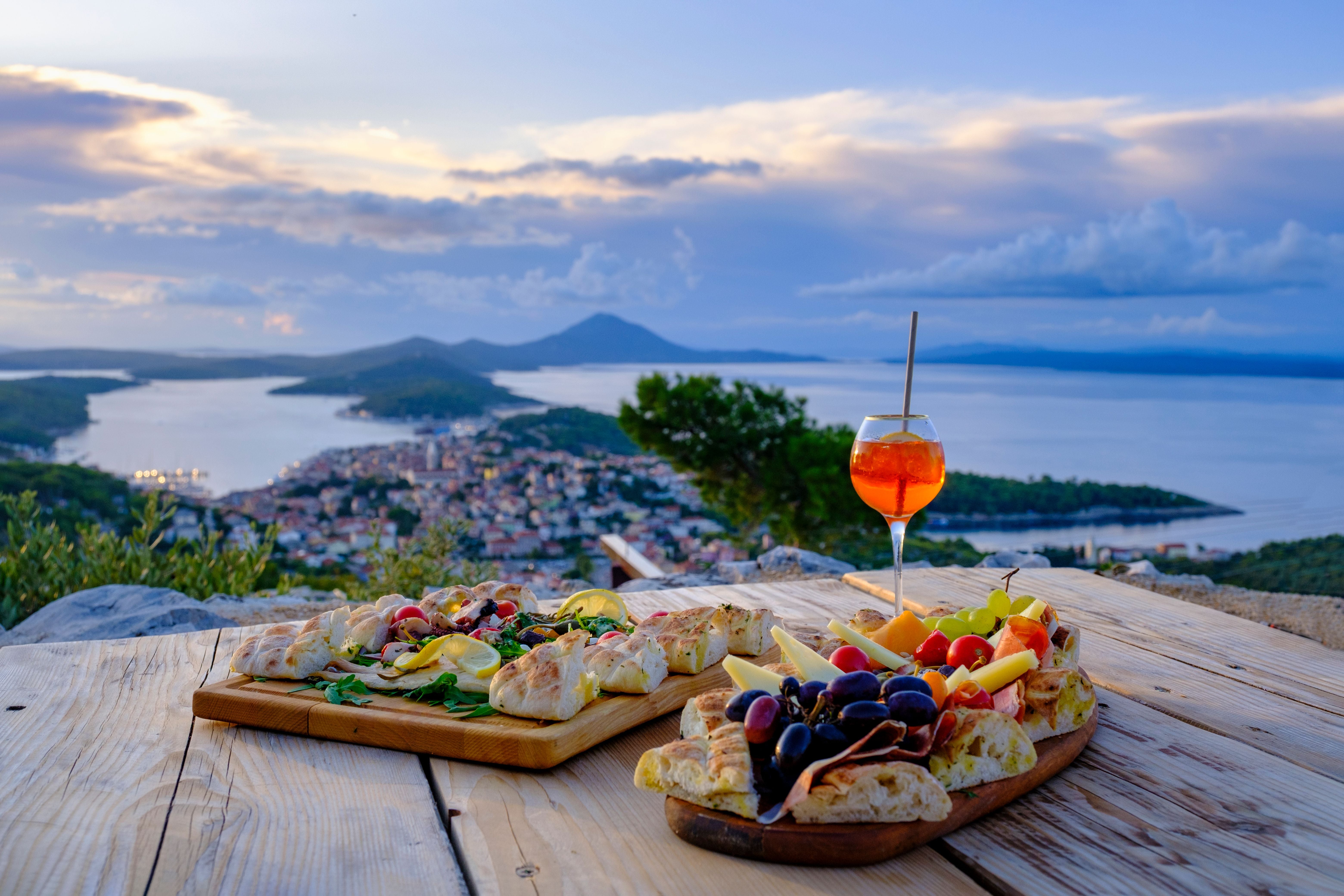 Vorspeisen und ein Getränk auf Holztisch mit Ausblick auf kroatische Küstenstadt und Meer.