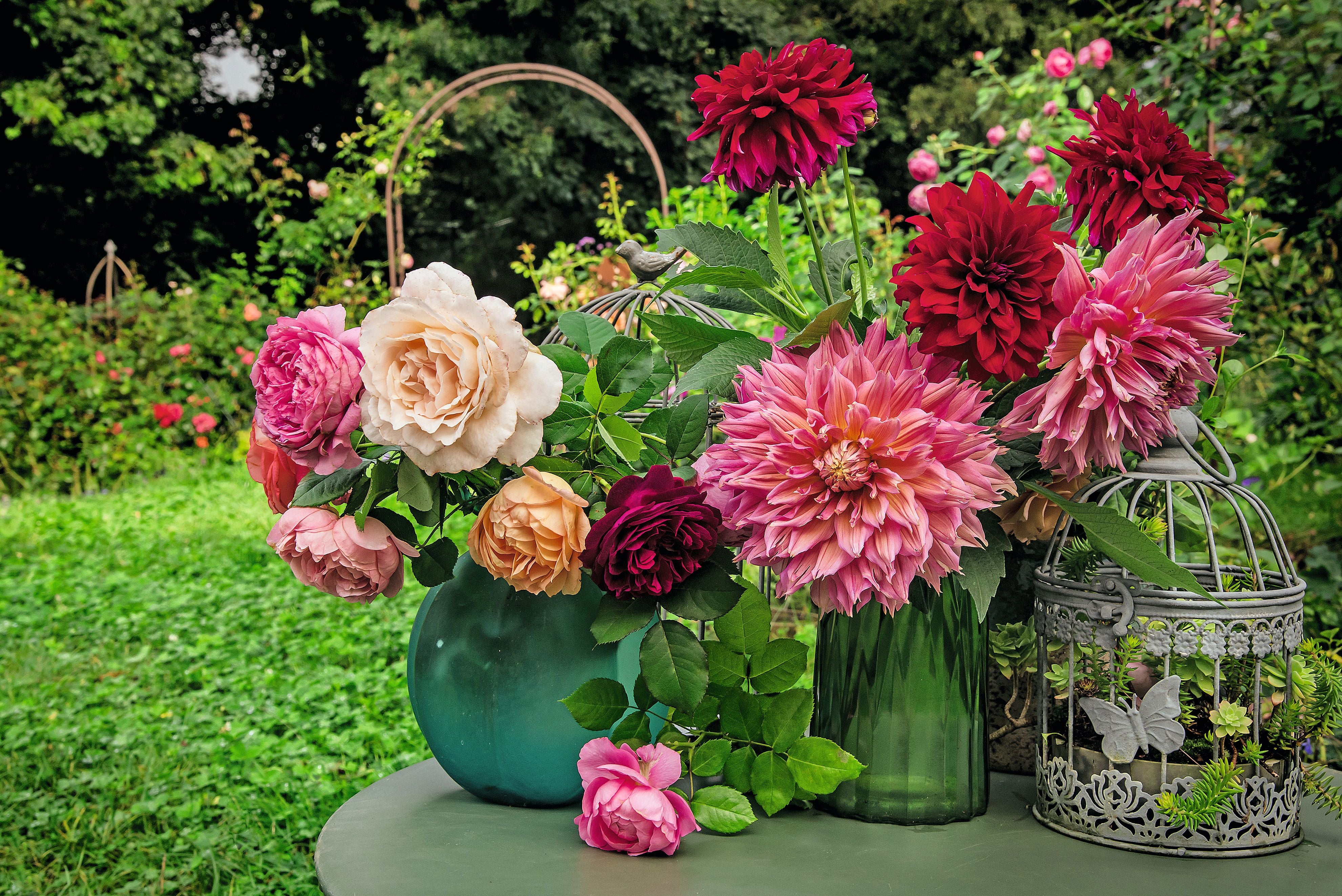 Bunter Blumenstrauß mit Rosen und Dahlien in Vasen auf einem Gartentisch im Sommer.