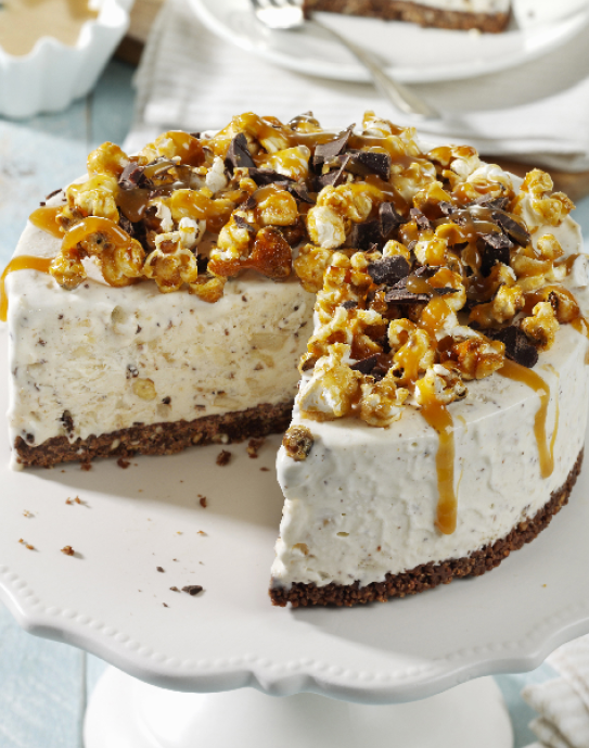 Eistorte mit Karamellpopcorn, Schokostückchen und Karamellsauce auf Tortenplatte.