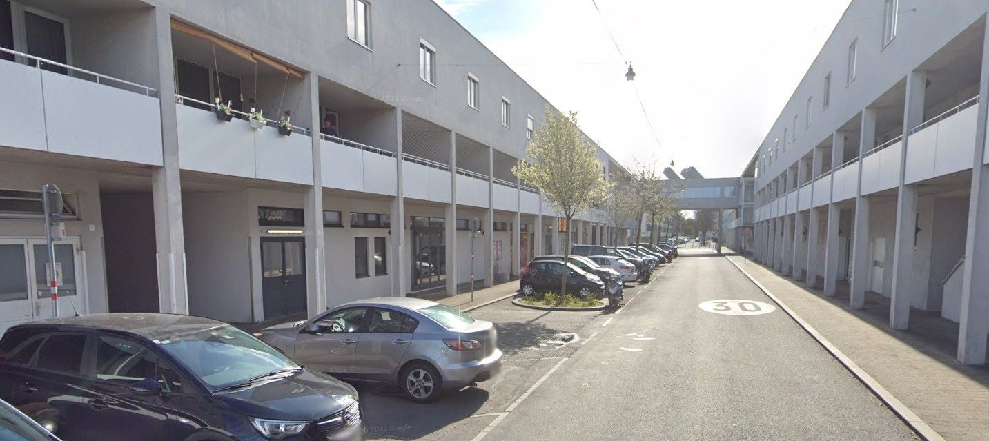 Moderne Wohnhäuser mit Balkonen, parkende Autos und Bäume entlang der Eibengasse im 22. Bezirk.