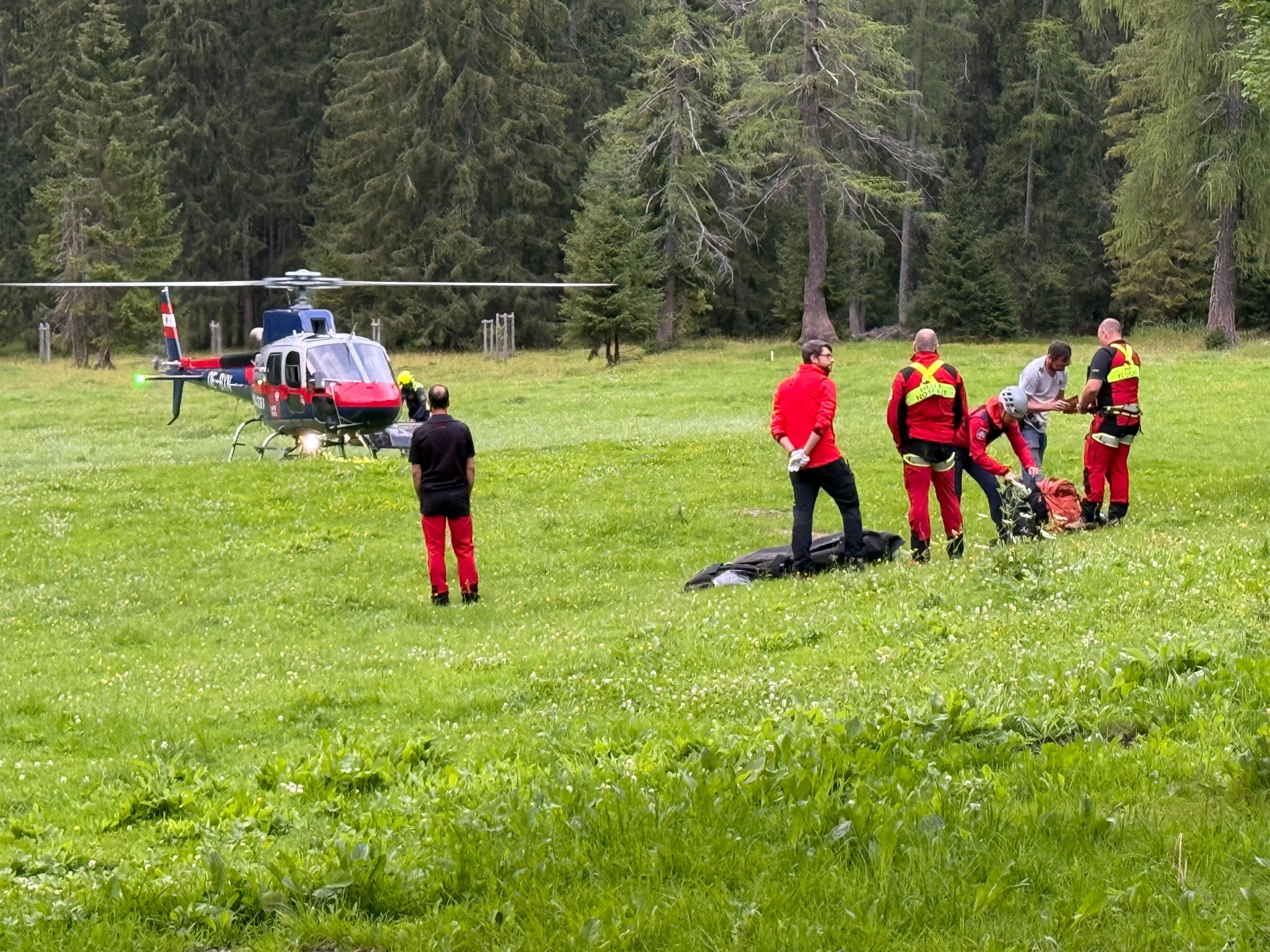 Rettungsteam mit Hubschrauber versorgt verletzte Person auf einer Wiese im Wald.