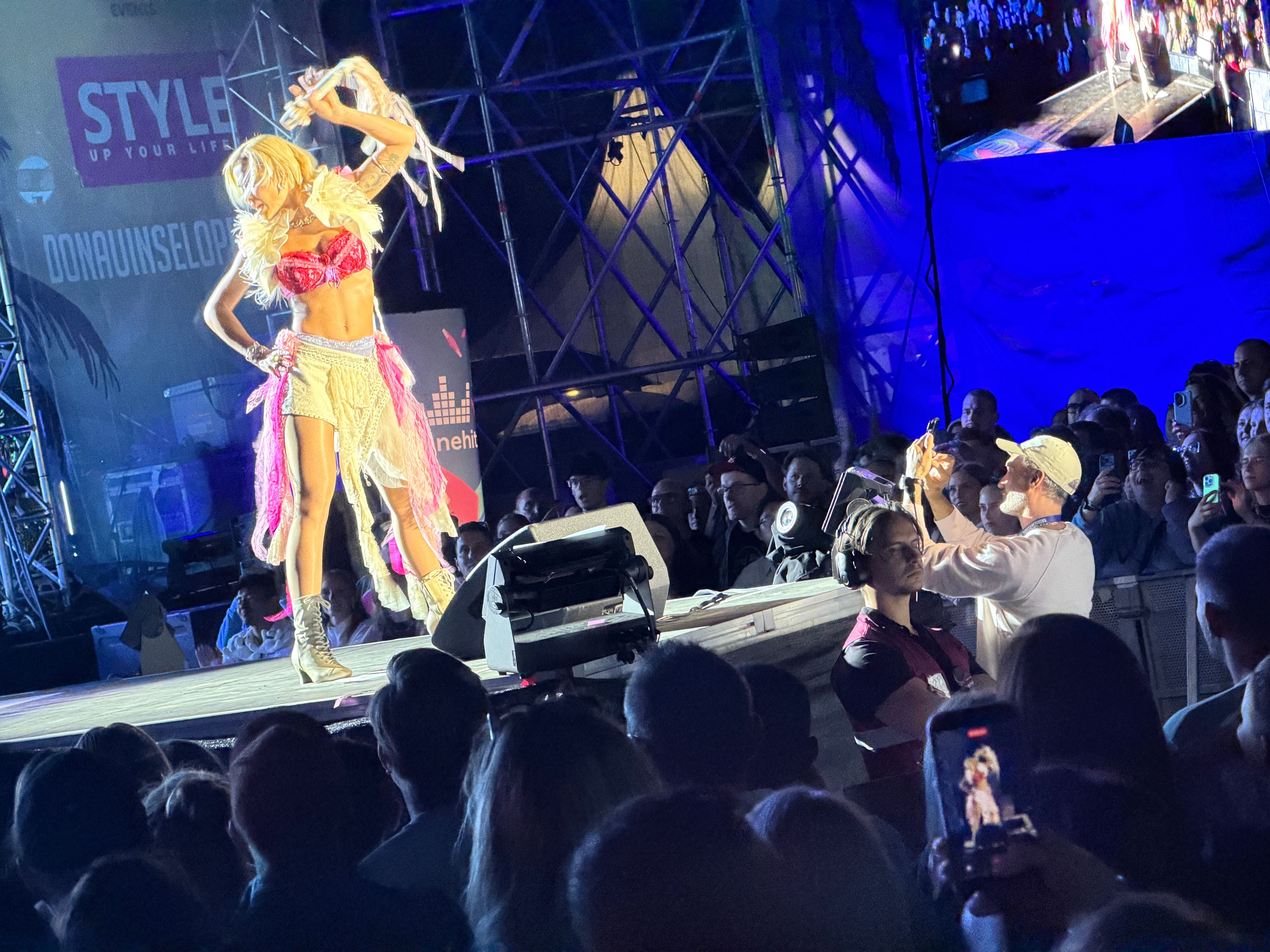 Rita Ora tritt auf einer hell beleuchteten Bühne vor einem begeisterten Publikum auf.