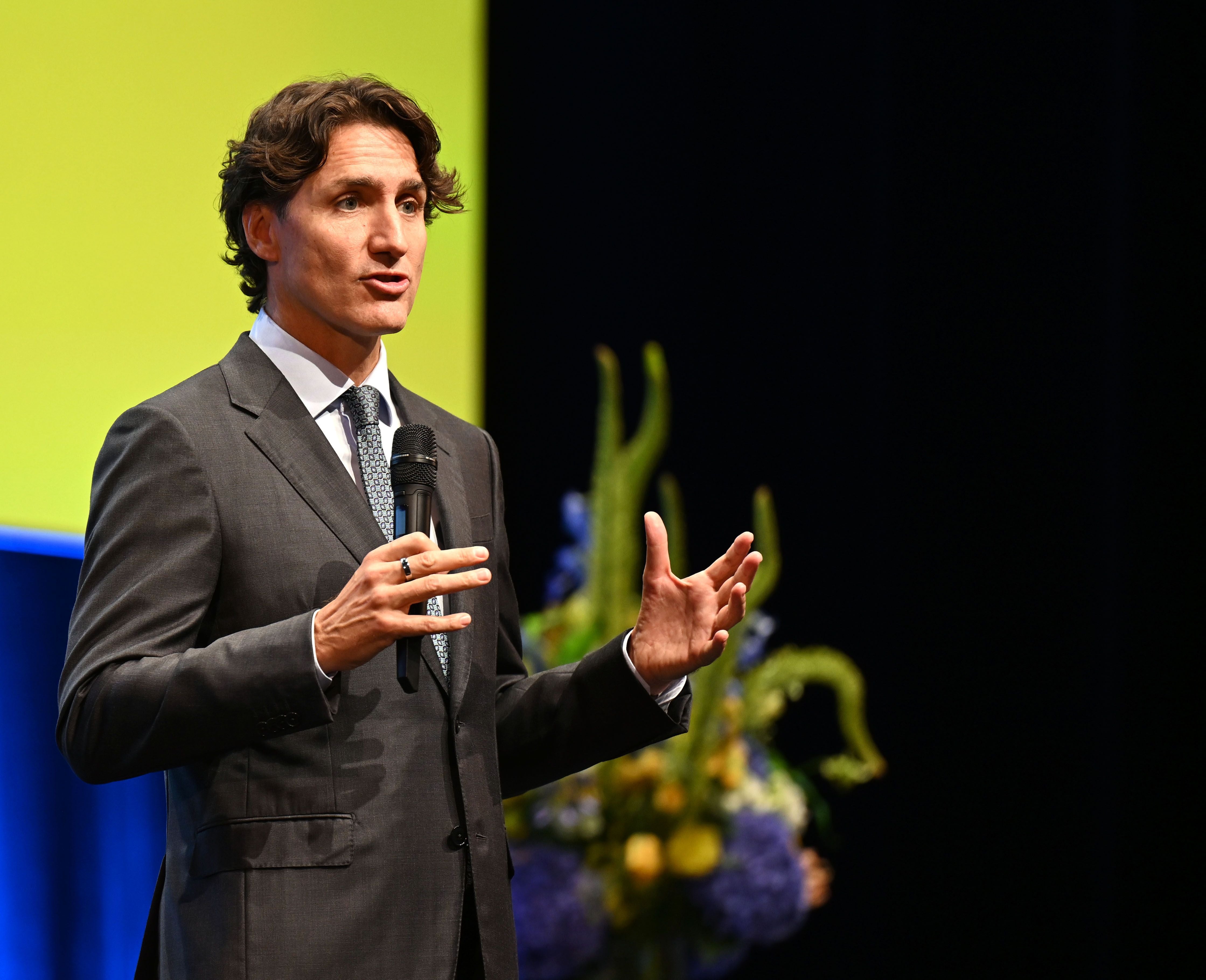 Ein Mann im Anzug hält eine Keynote und spricht mit einem Mikrofon auf einer Bühne.