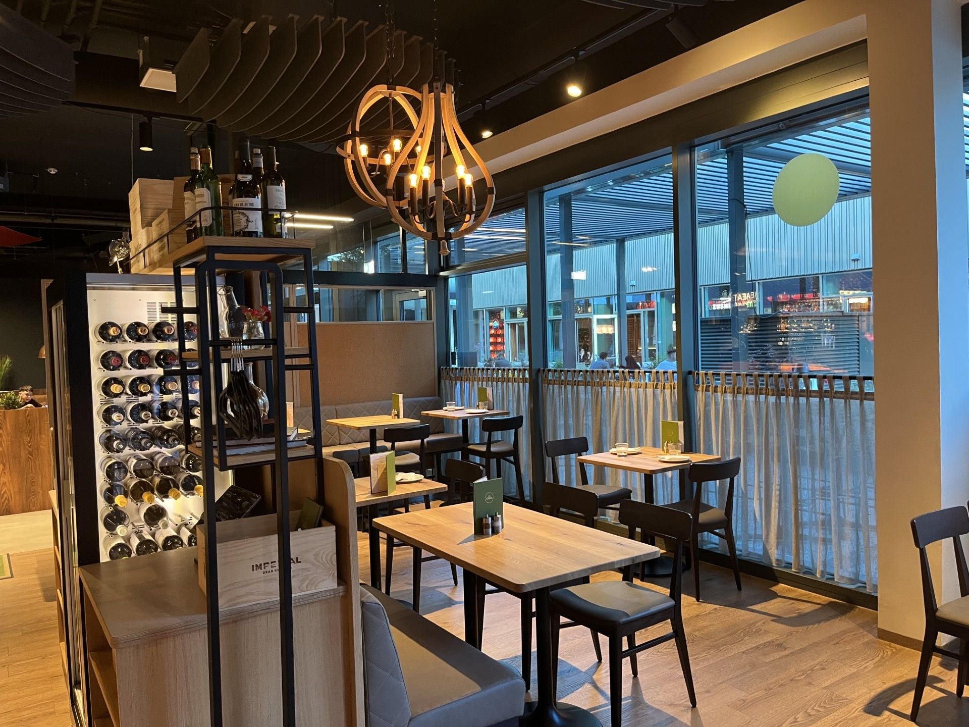 Modernes Restaurant mit Holzdekor, Weinauslage und großen Fenstern mit Blick nach draußen.