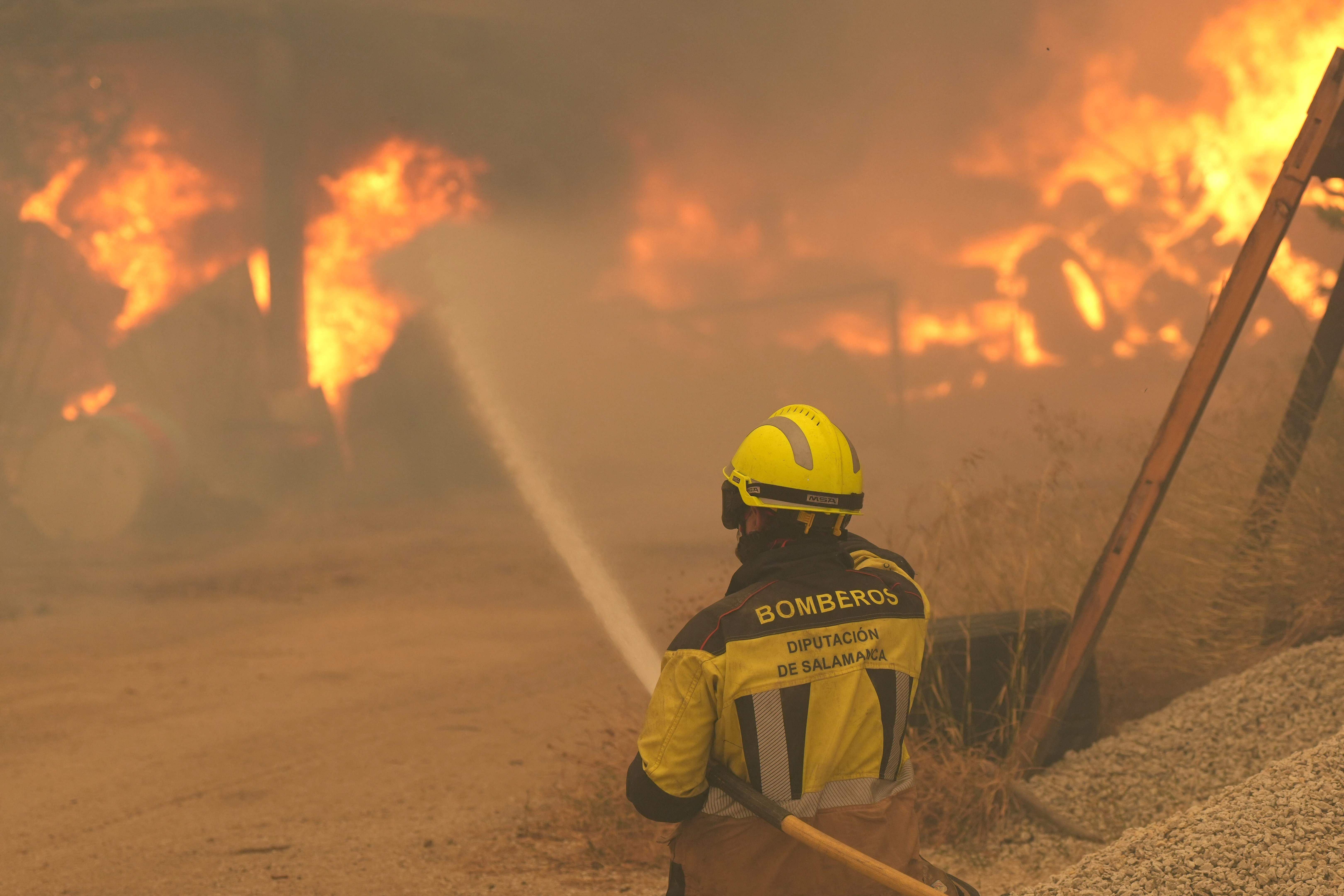 Ein Feuerwehrmann bekämpft einen Großbrand mit Wasser vor lodernden Flammen und Rauch.