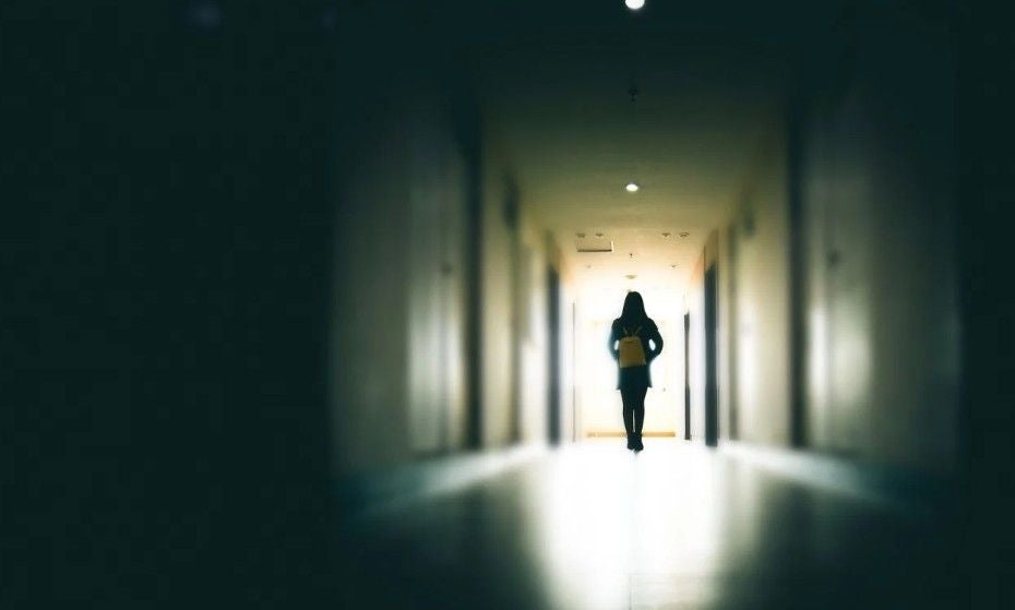 Silhouette einer Person läuft durch einen dunklen, leeren Flur auf eine helle Tür zu.