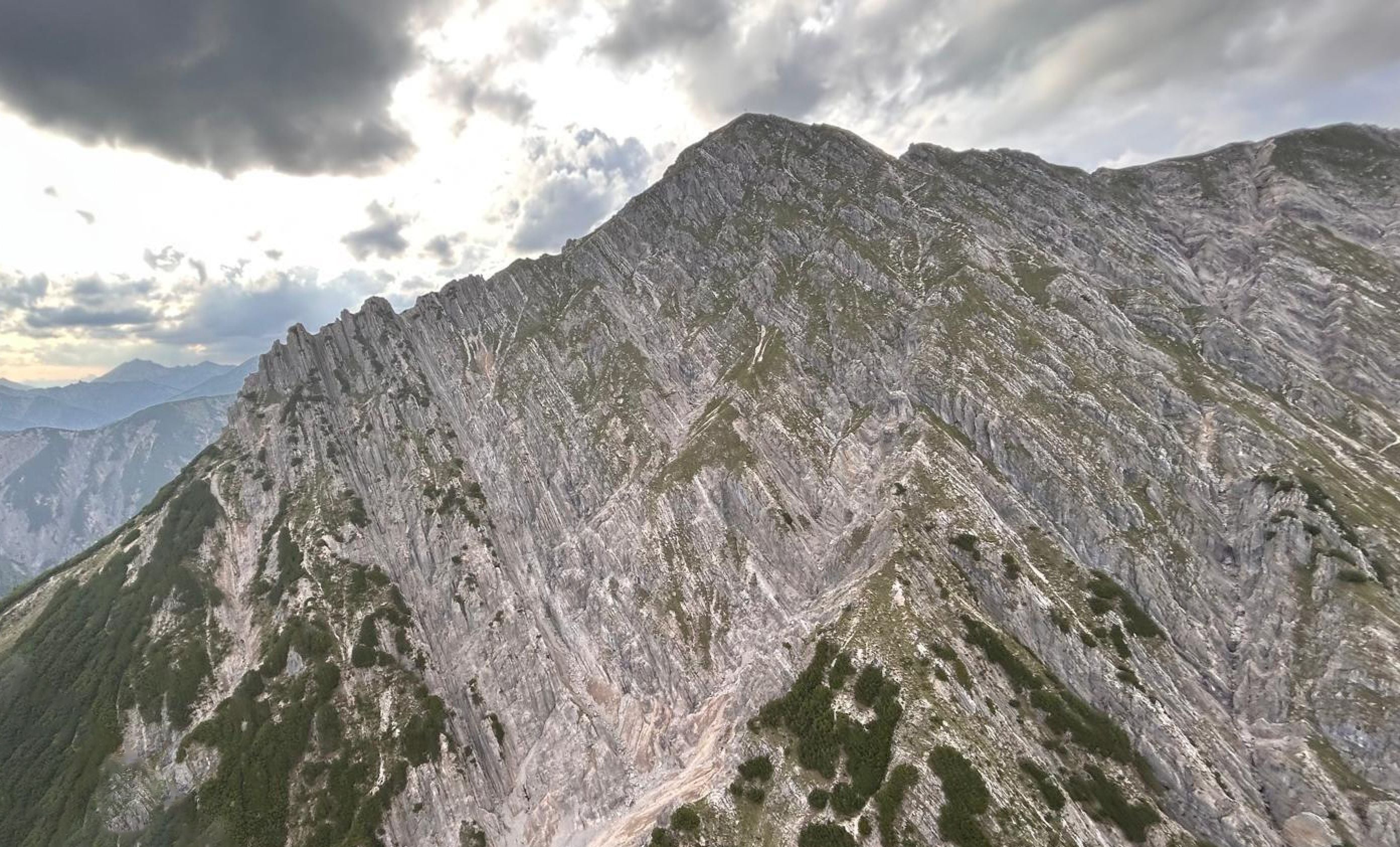 Steiler Bergrücken mit markanten Felsen und grünen Büschen unter bewölktem Himmel.