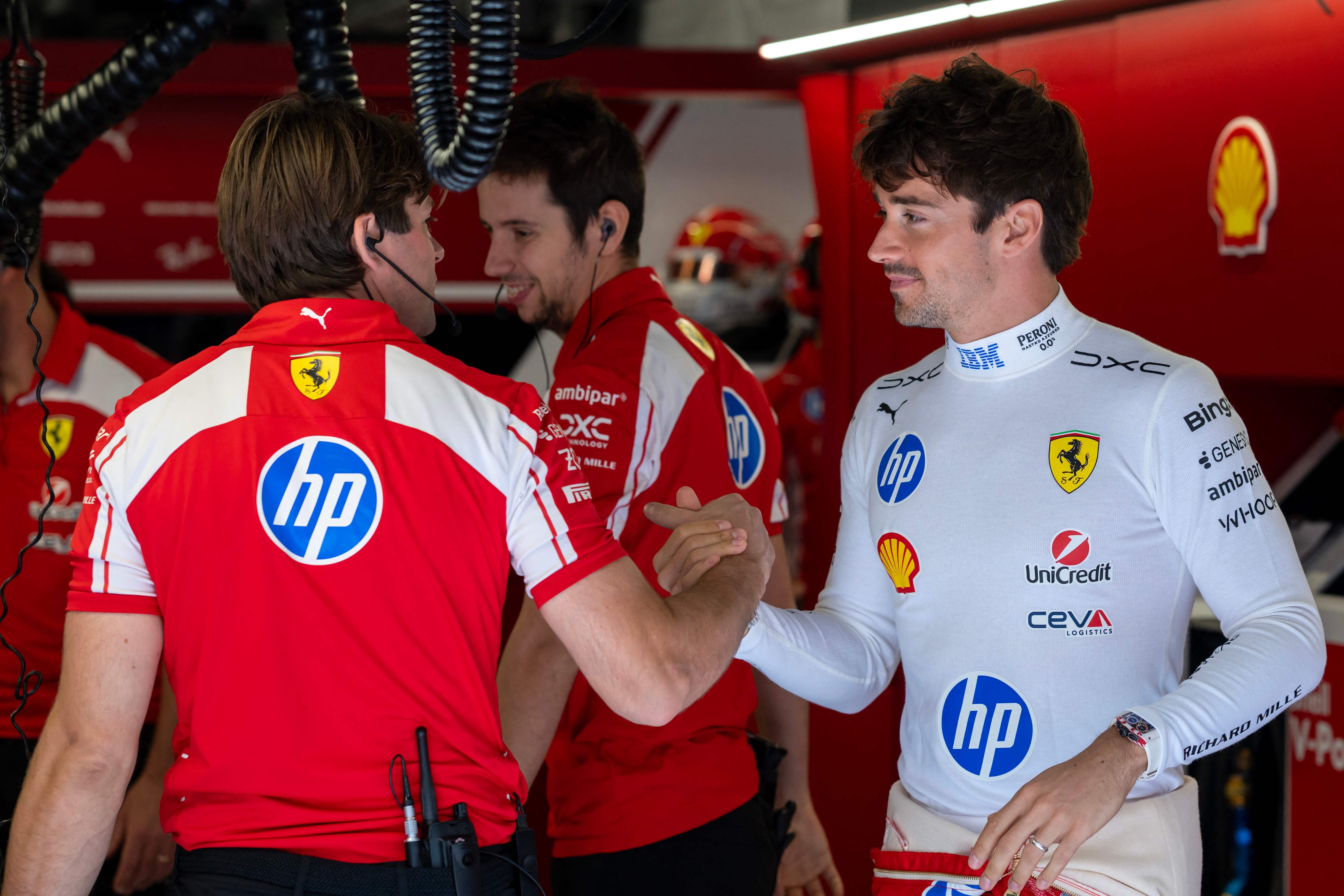 Charles Leclerc im weißen Ferrari-Rennanzug gibt einem Teammitglied in rot-weißer Teamkleidung in der Box die Hand.