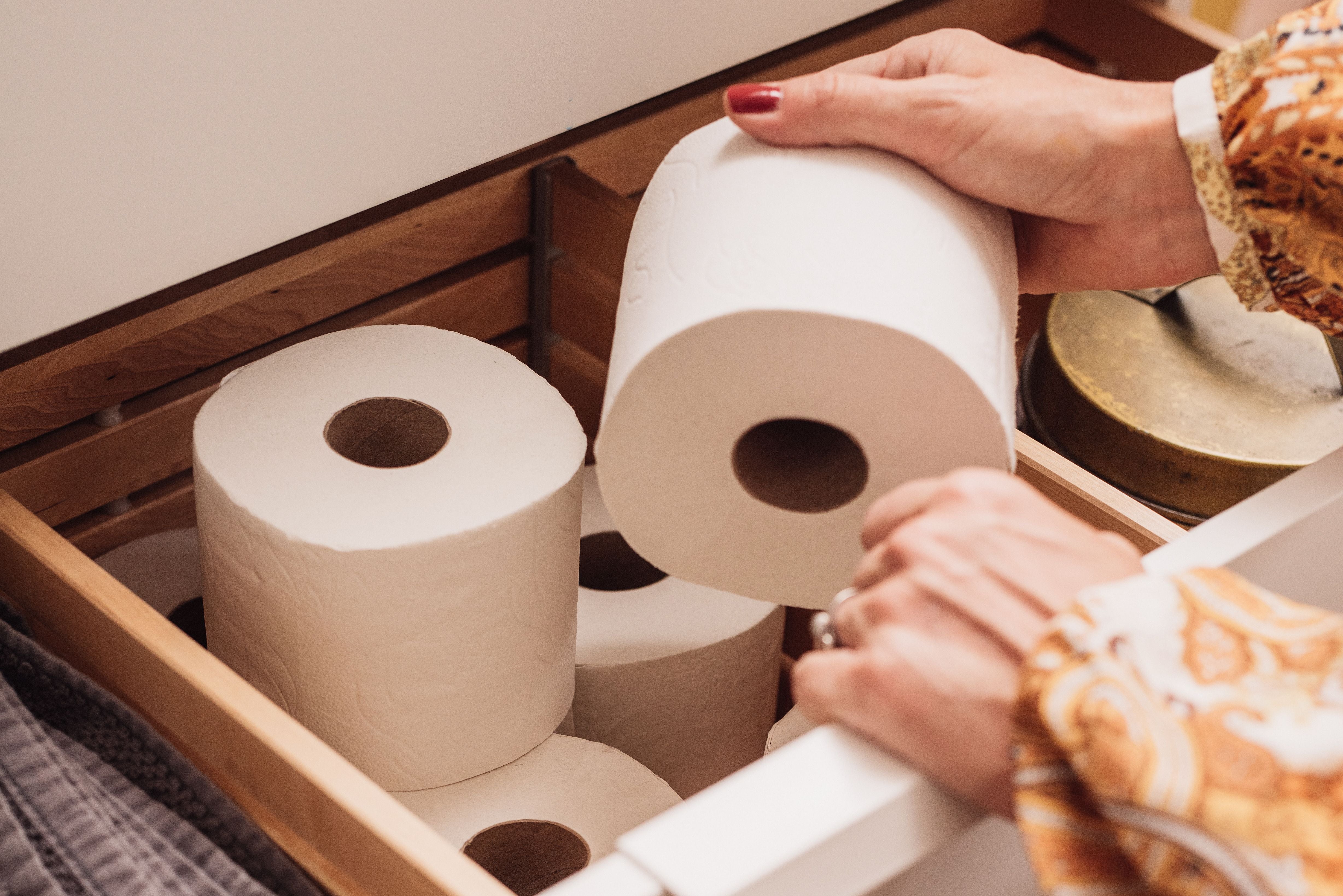 Frau nimmt eine Rolle Toilettenpapier aus einer Schublade mit mehreren Rollen.