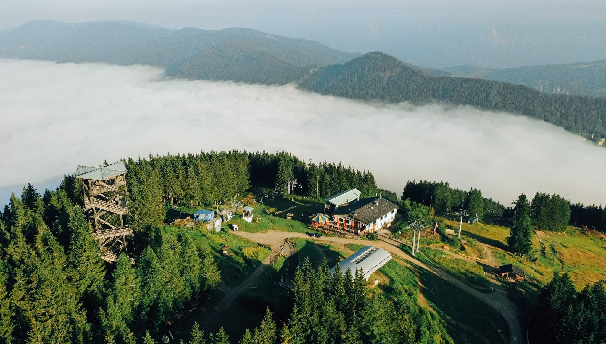 Aussichtsturm und Gebäude am Semmering, umgeben von Wald und Nebel mit Bergen im Hintergrund.